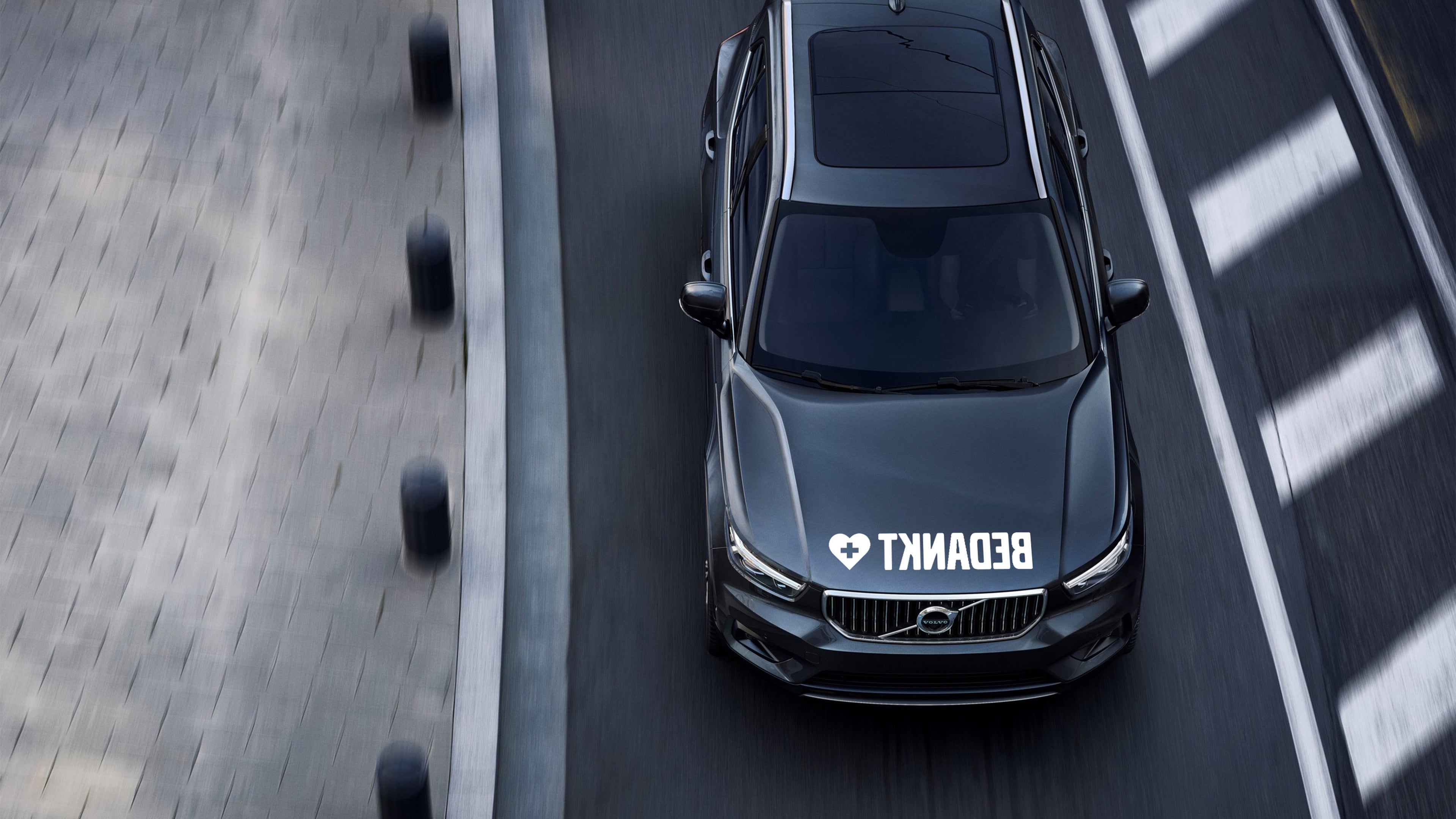 Een zwarte Volvo XC60 op straat in de stad rijdt, wordt van bovenaf bekeken. Op de voorruit staat een grote witte "BECAKIT"