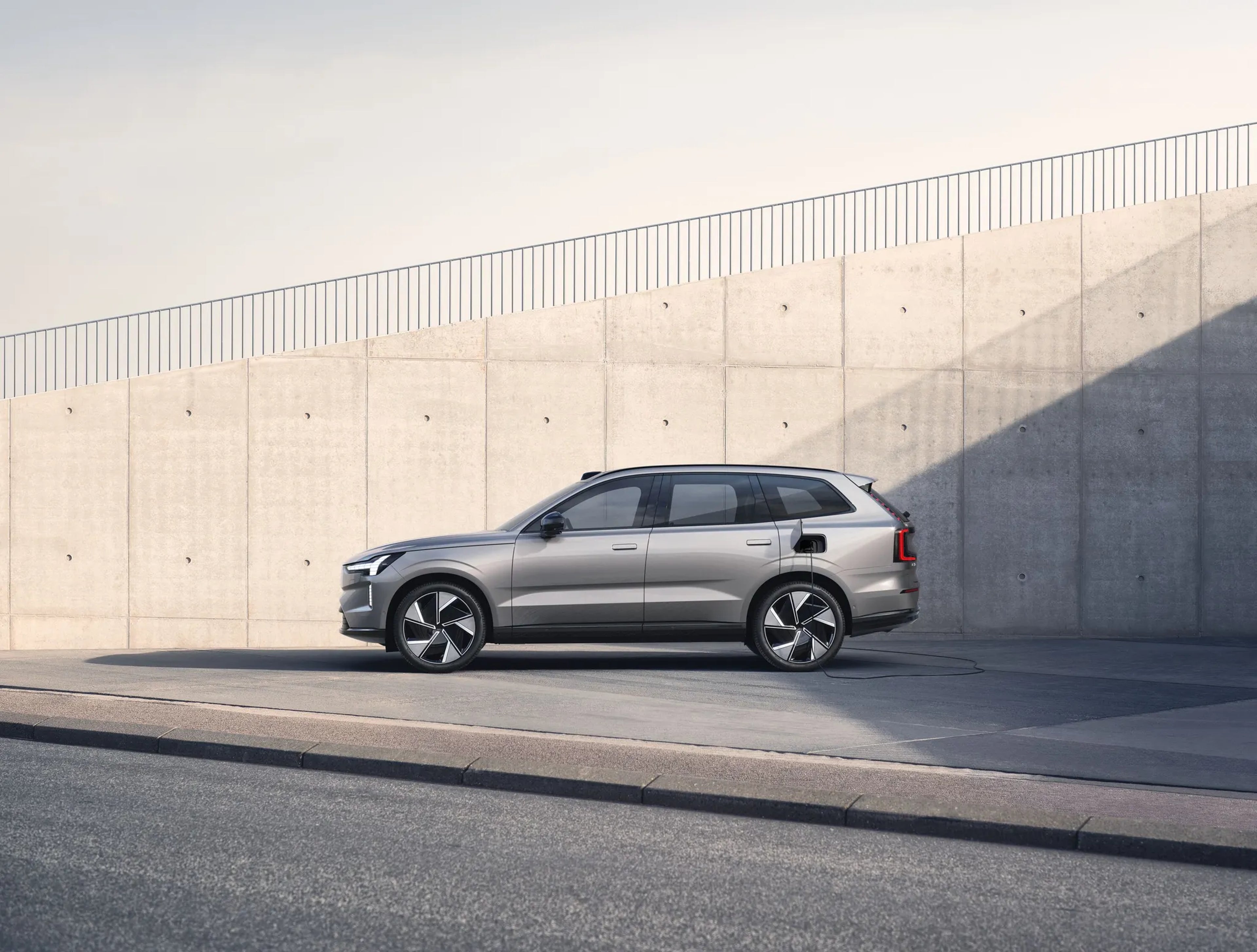 En kvindelig fører af en firmabil oplader en Volvo-EX90 ved en vægmonteret lader uden for en murstensbygning.