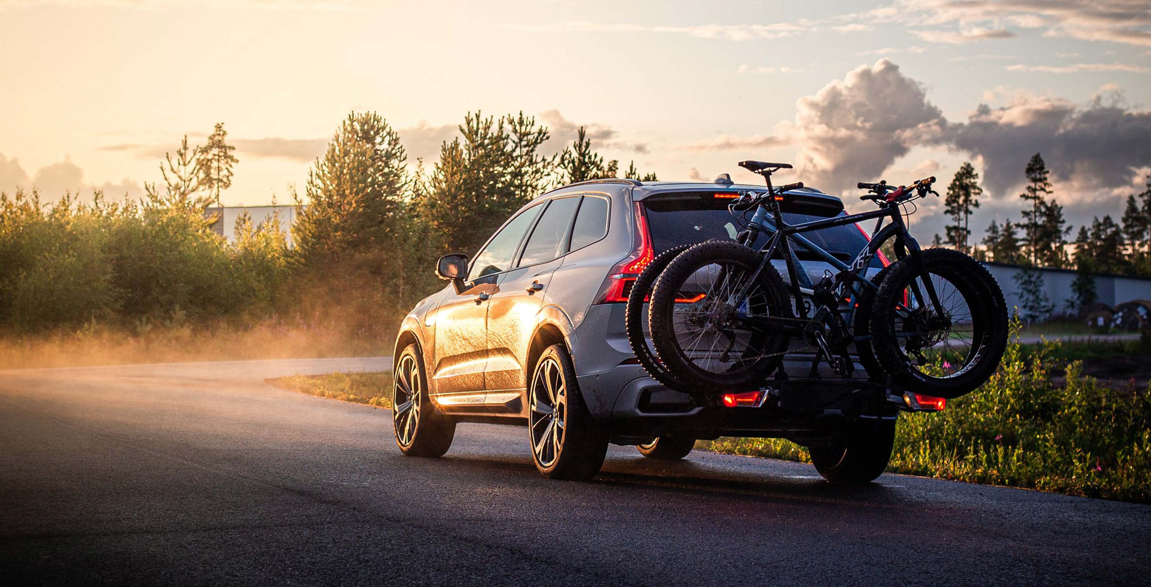 Harmaa XC60, jonka vetokoukkuun on kiinnitetty polkupyöräteline ja kaksi maaastopyörää ajaa usvaisella tiellä auringonlaskussa.