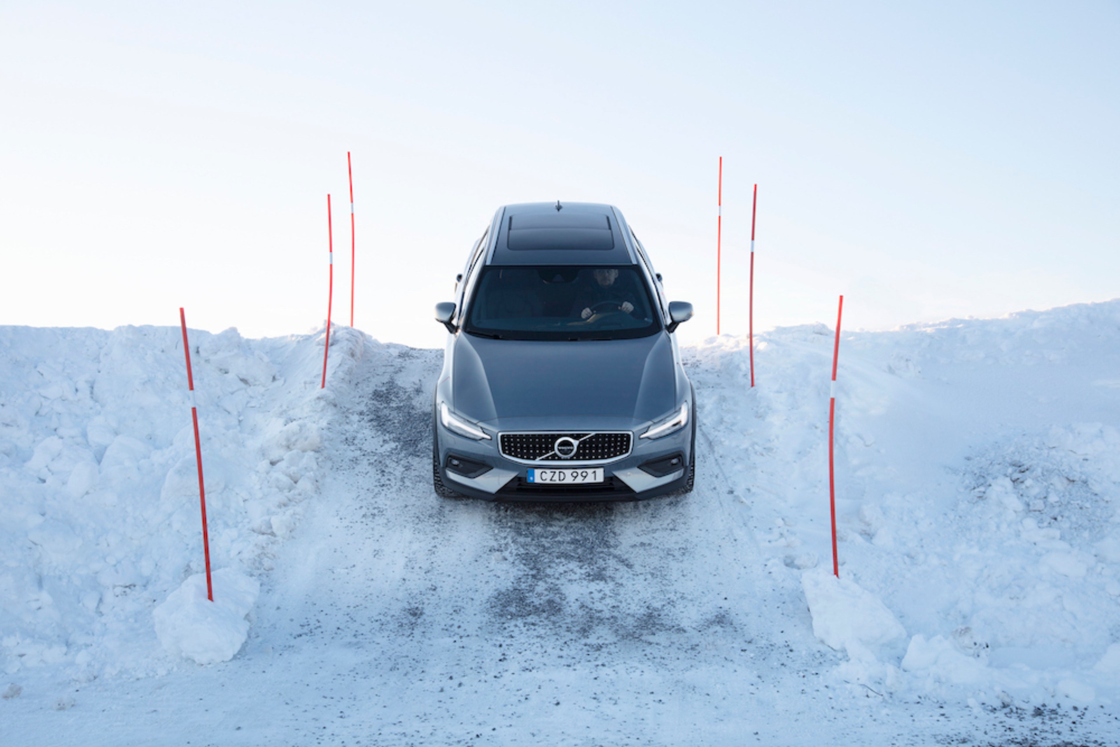 Volvo V60 Cross Country fährt über einen schneebedeckten Hügel inmitten eines Slalom Pakours