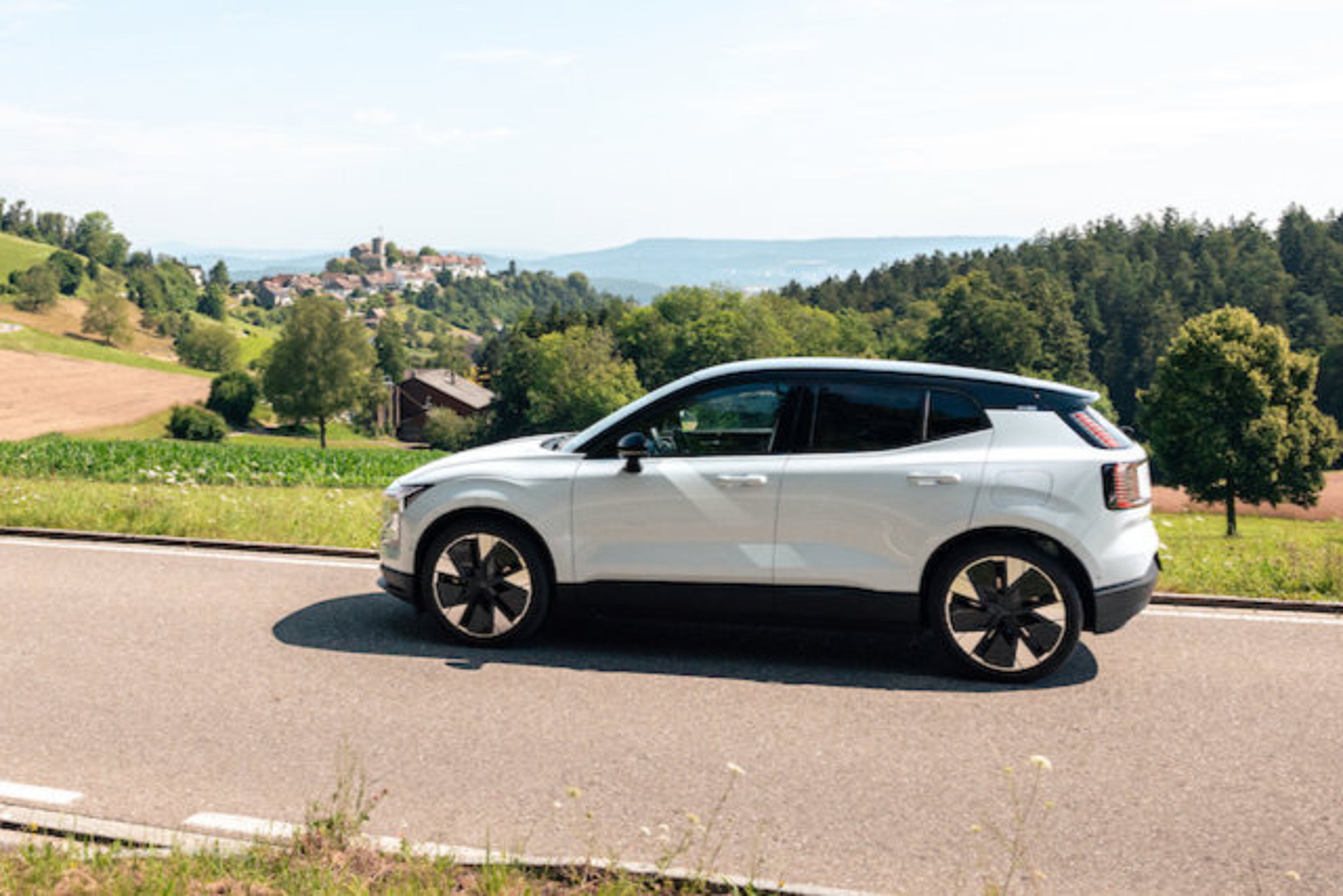 Vue latérale d'une Volvo EX30 blanche sur une route de campagne.