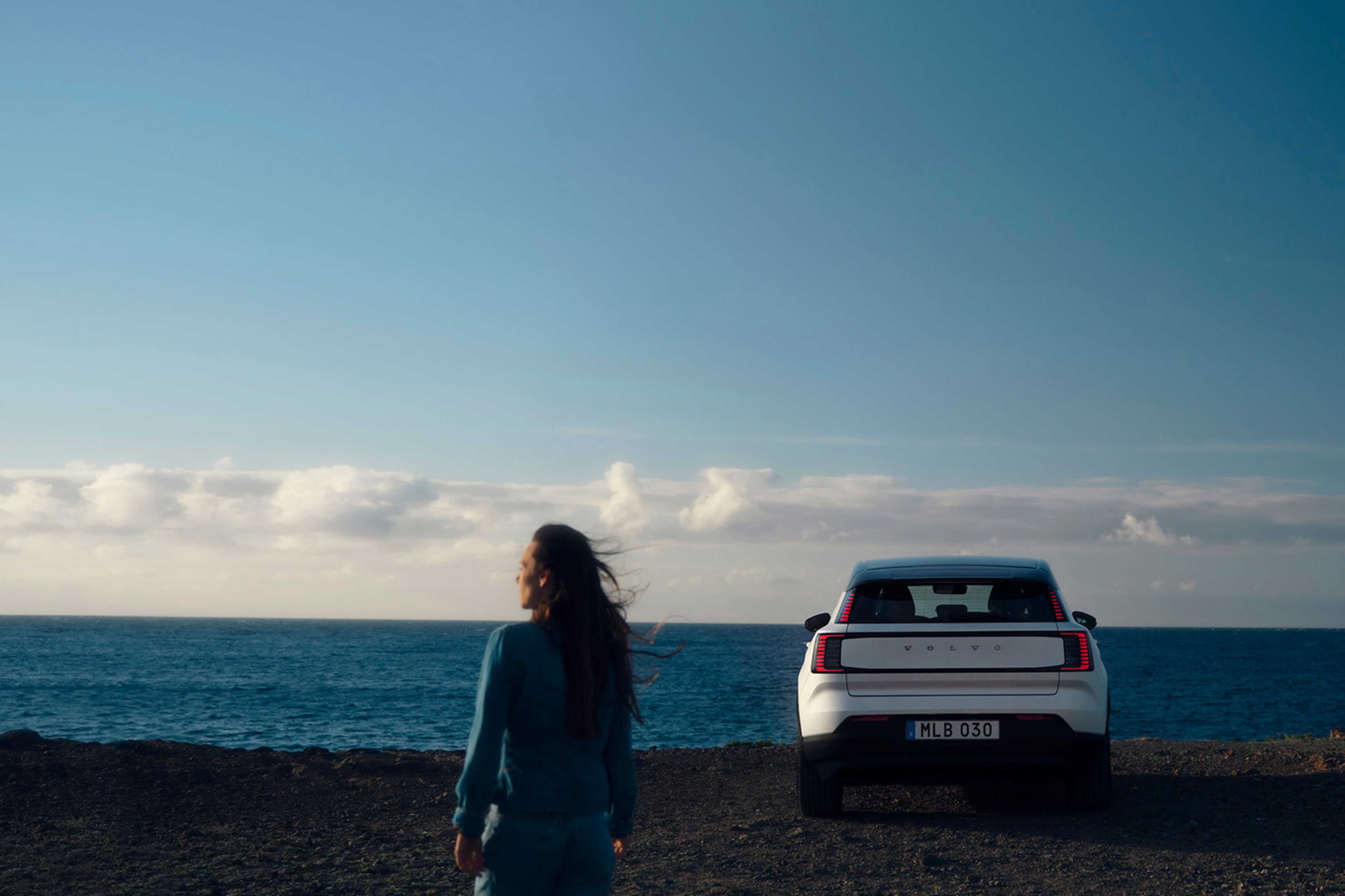 obrázok kampane Ocean Race 2025, na ktorom žena stojí pri oceáne vedľa auta