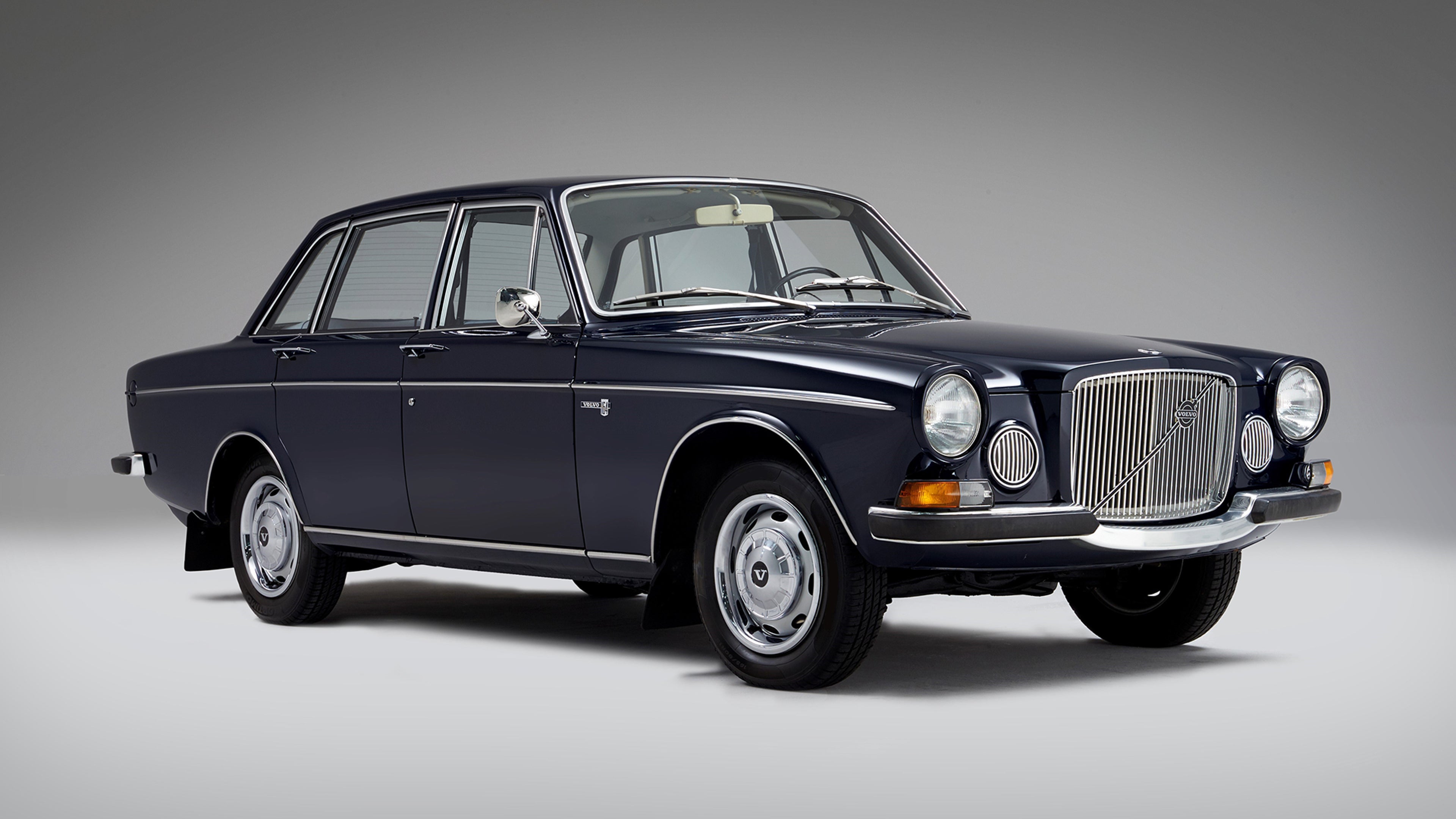 Volvo 164 سيدان كلاسيكية باللون الأزرق الداكن مع شبكة كروم وأضواء أمامية مستديرة، متوقفة ومصقولة بتصميم صندوقي عتيق وأغطية محاور فضية