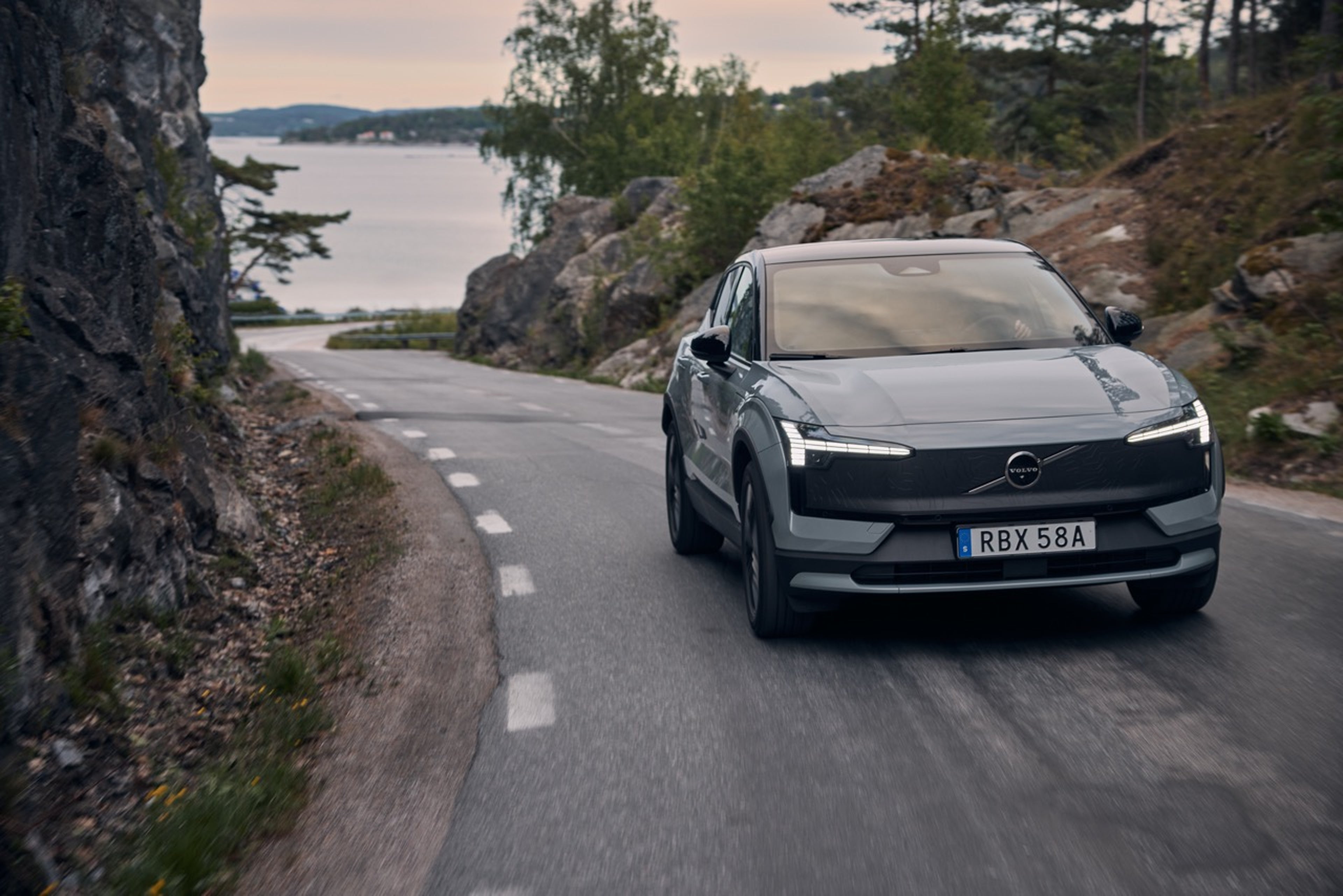 EX30 Cross Country manejando por una carretera rural sueca con el mar en la distancia.
