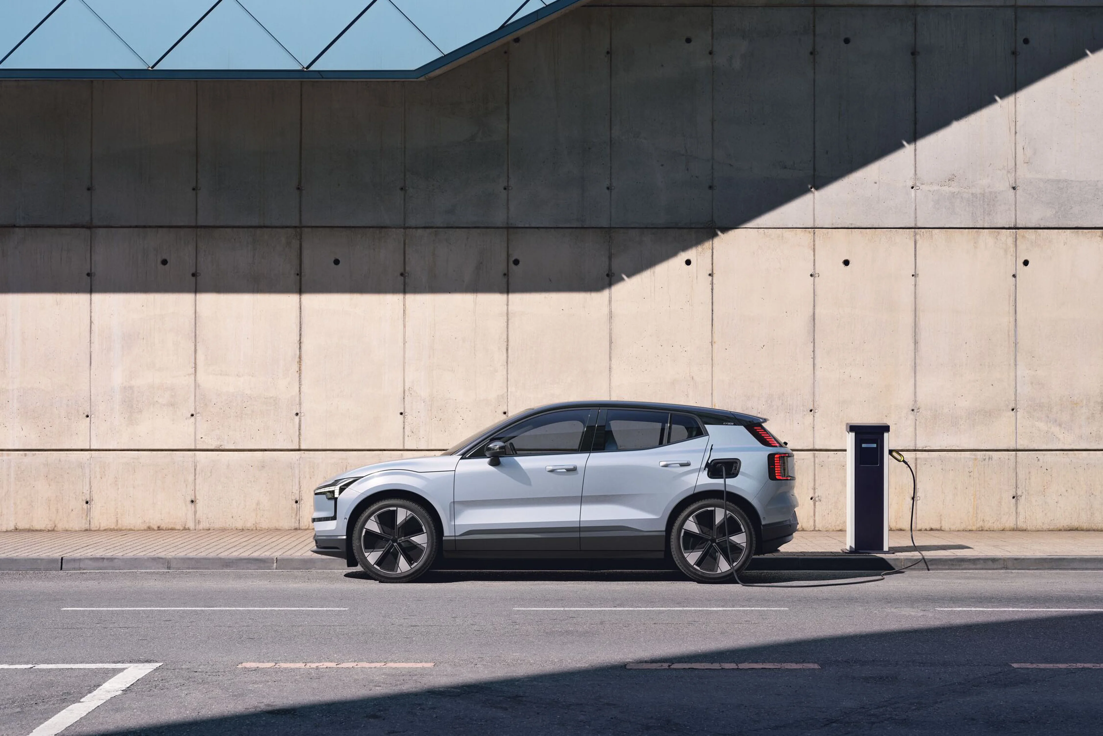 Volvo EX30 zaparkované pri betónovej stene a pripojené na nabíjačku.