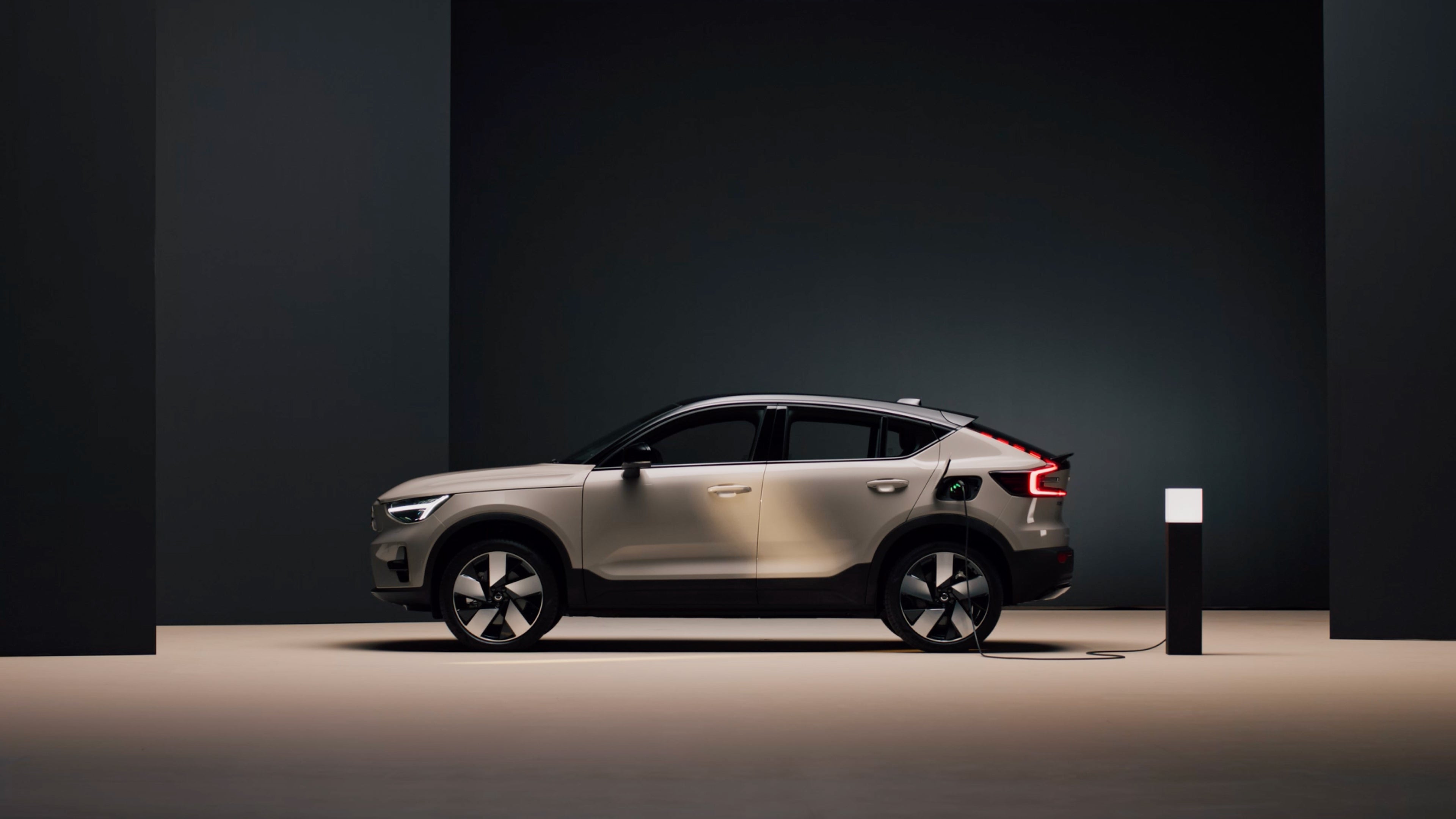 Conductrice d’une voiture de société chargeant un Volvo EX90 à une station murale à l’extérieur d’un bâtiment en briques.