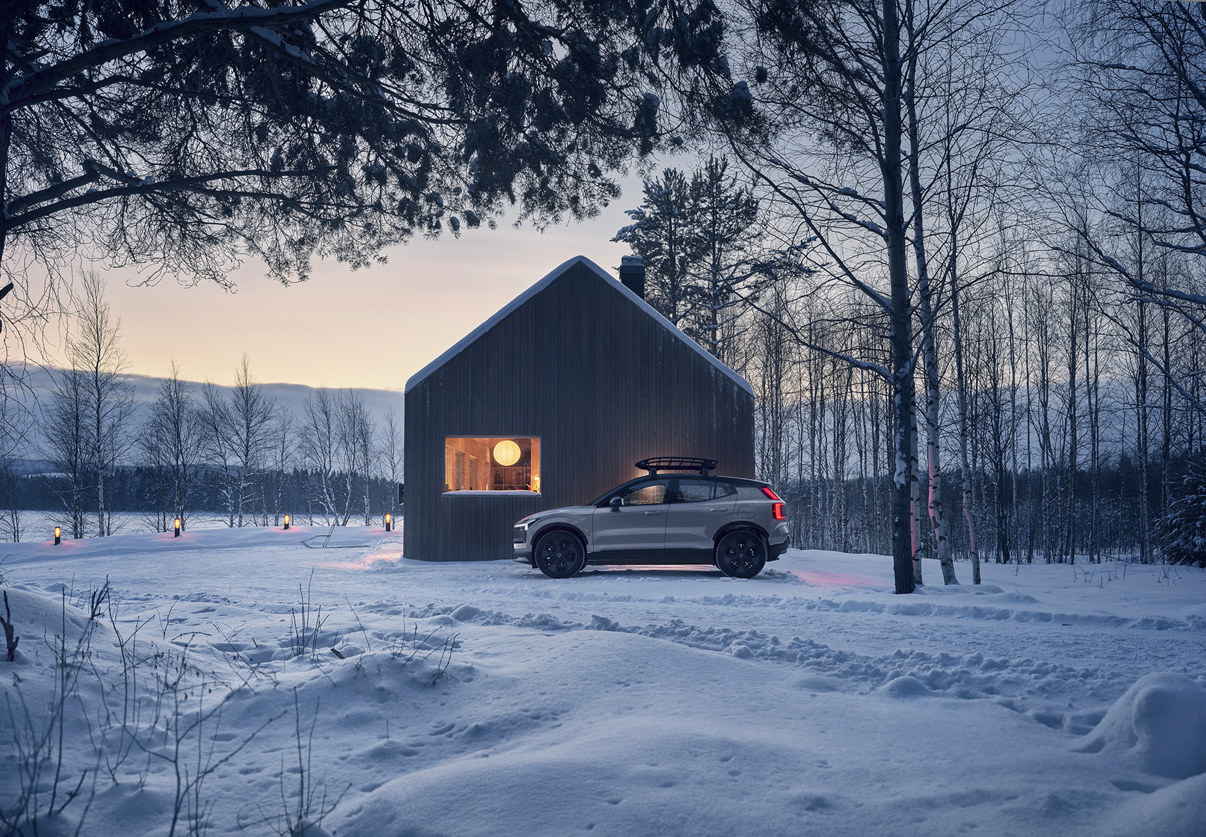 Volvo EX30 Cross Country parked near a winter cabin in Sweden, showcasing its rugged design with raised suspension and all-terrain wheels, ready for outdoor adventures.