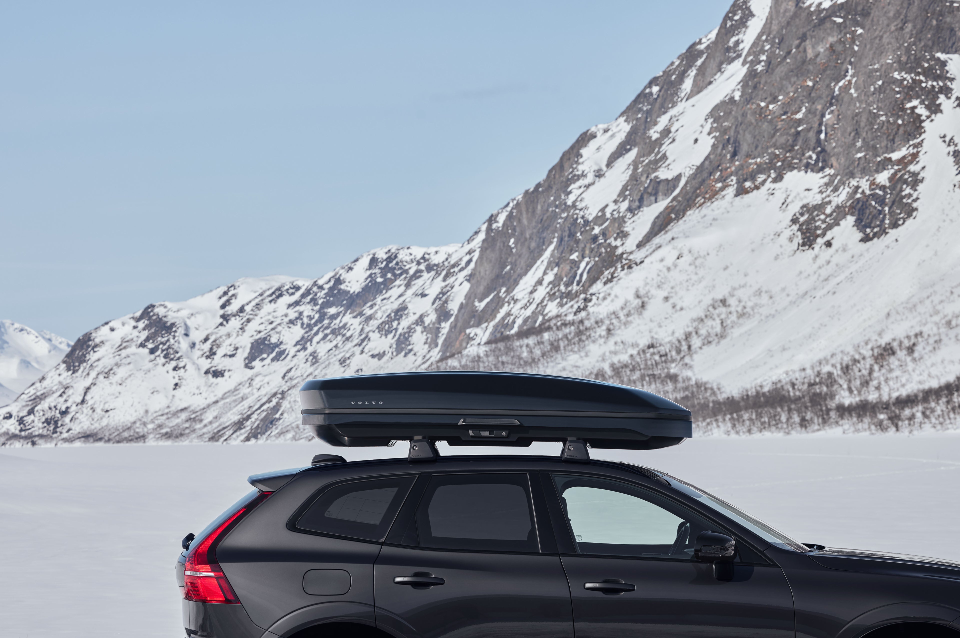 Volvo XC60 noire garée près d'une montagne enneigée.