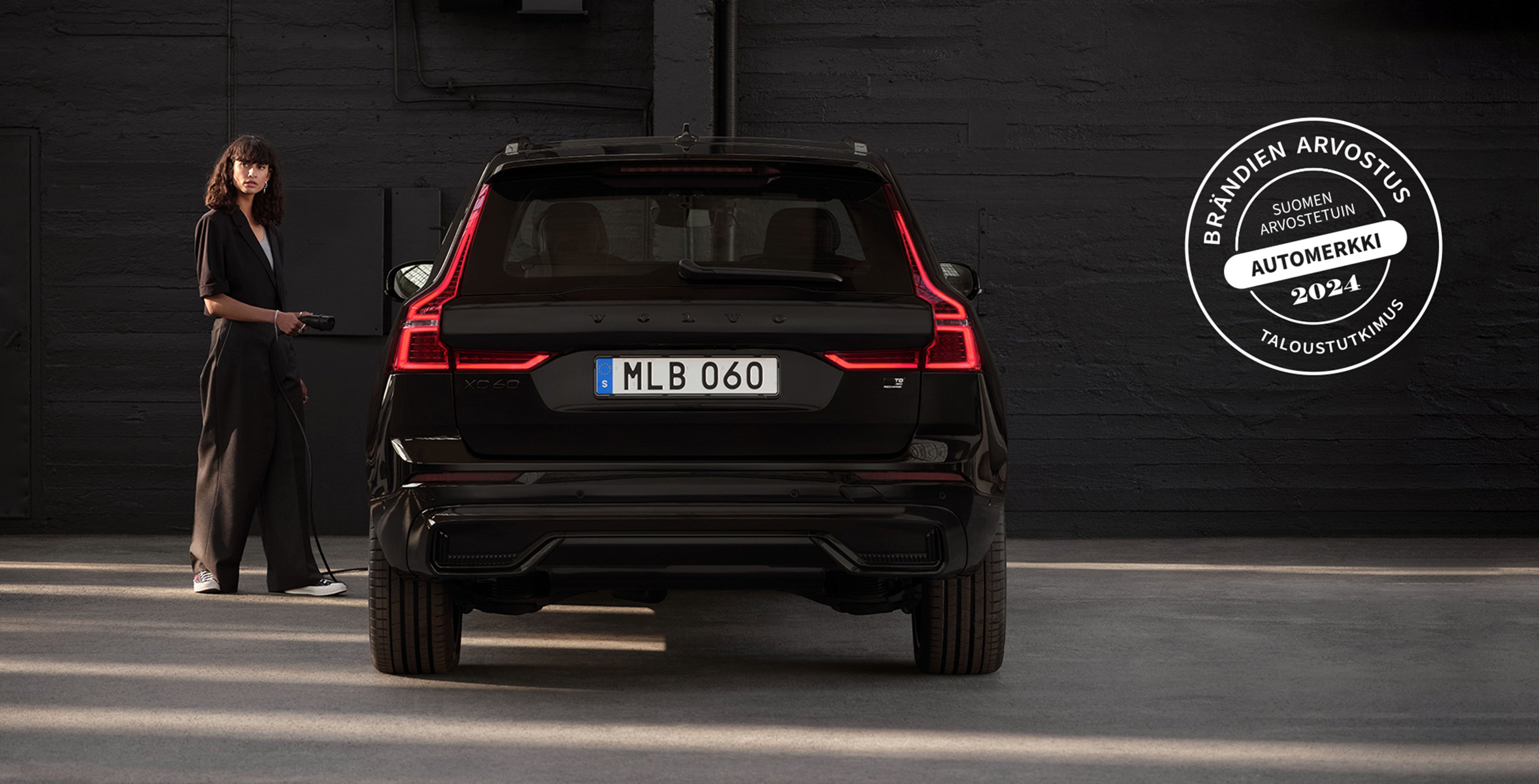 Mustiin pukeutunut nainen ja Volvo XC60 Black Edition -lataushybridi takaa päin kuvattuna.