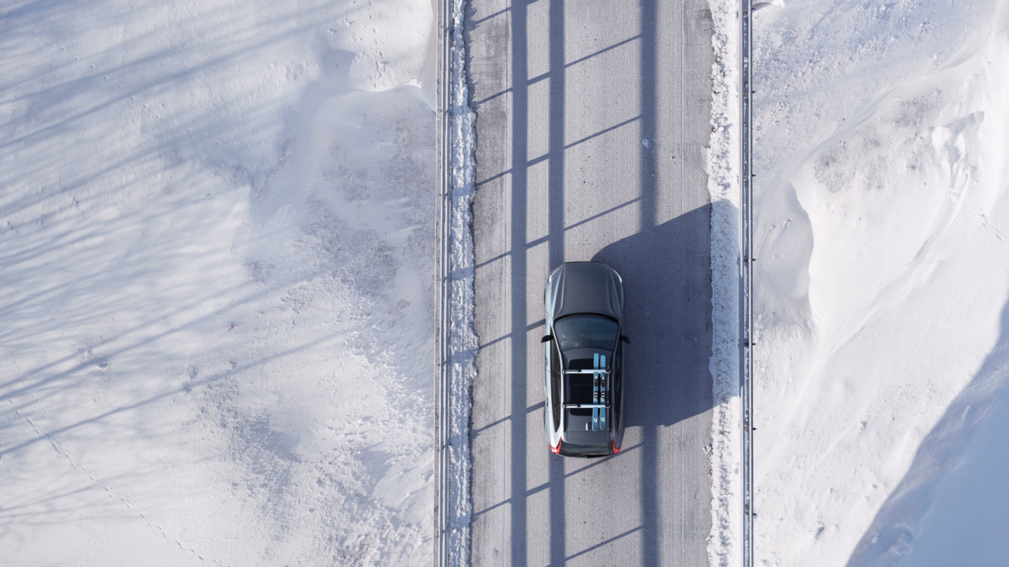 Thunder Grey -värinen Volvo XC60, jossa sukset kiinnitettynä taakkatelineisiin, ajaa lumisella maantiellä.