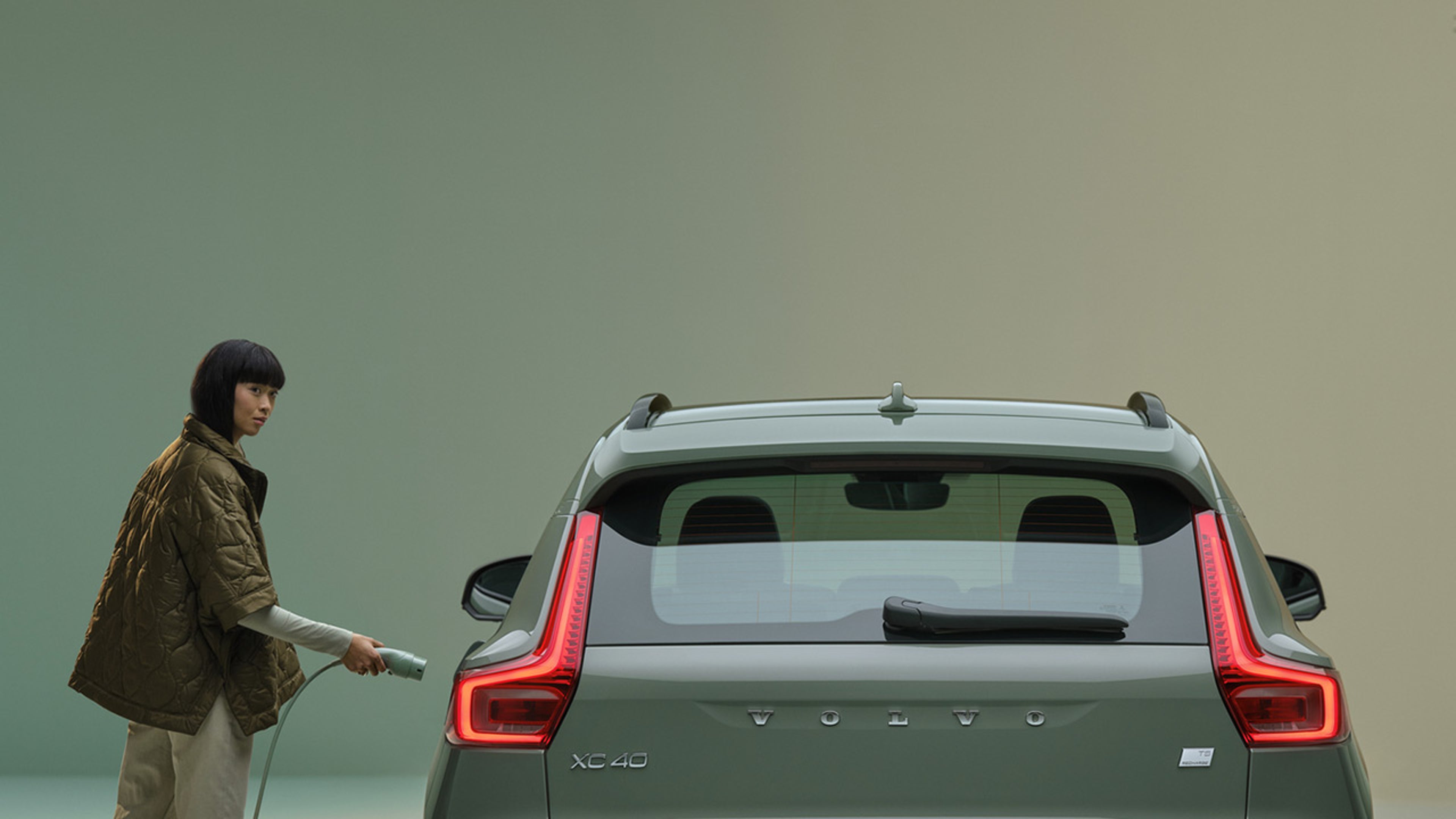 Une femme en manteau vert recharge une Volvo XC40 Recharge.