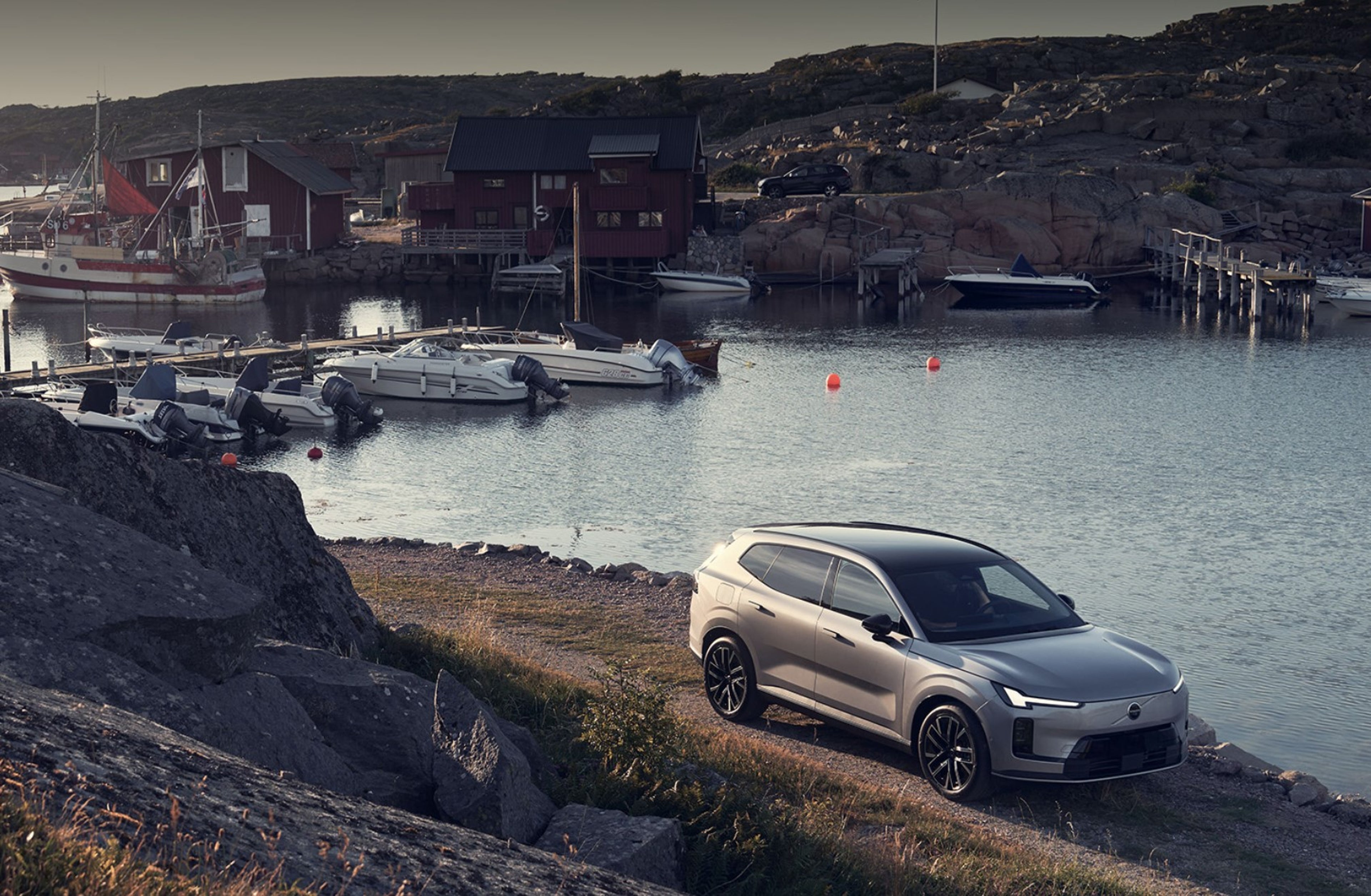 A silver SUV parked near a rocky shoreline with a small harbor in the background.