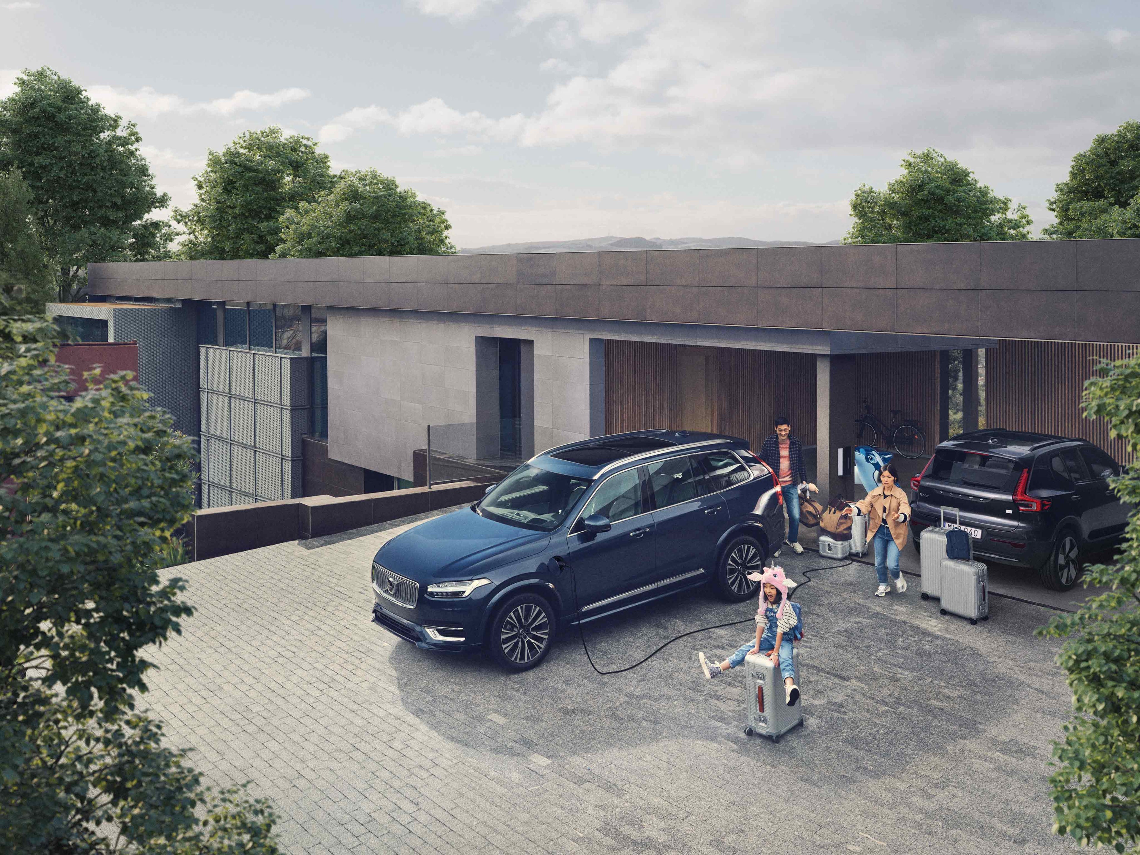 Family with luggage and a Denim Blue Volvo XC90 Recharge on a driveway