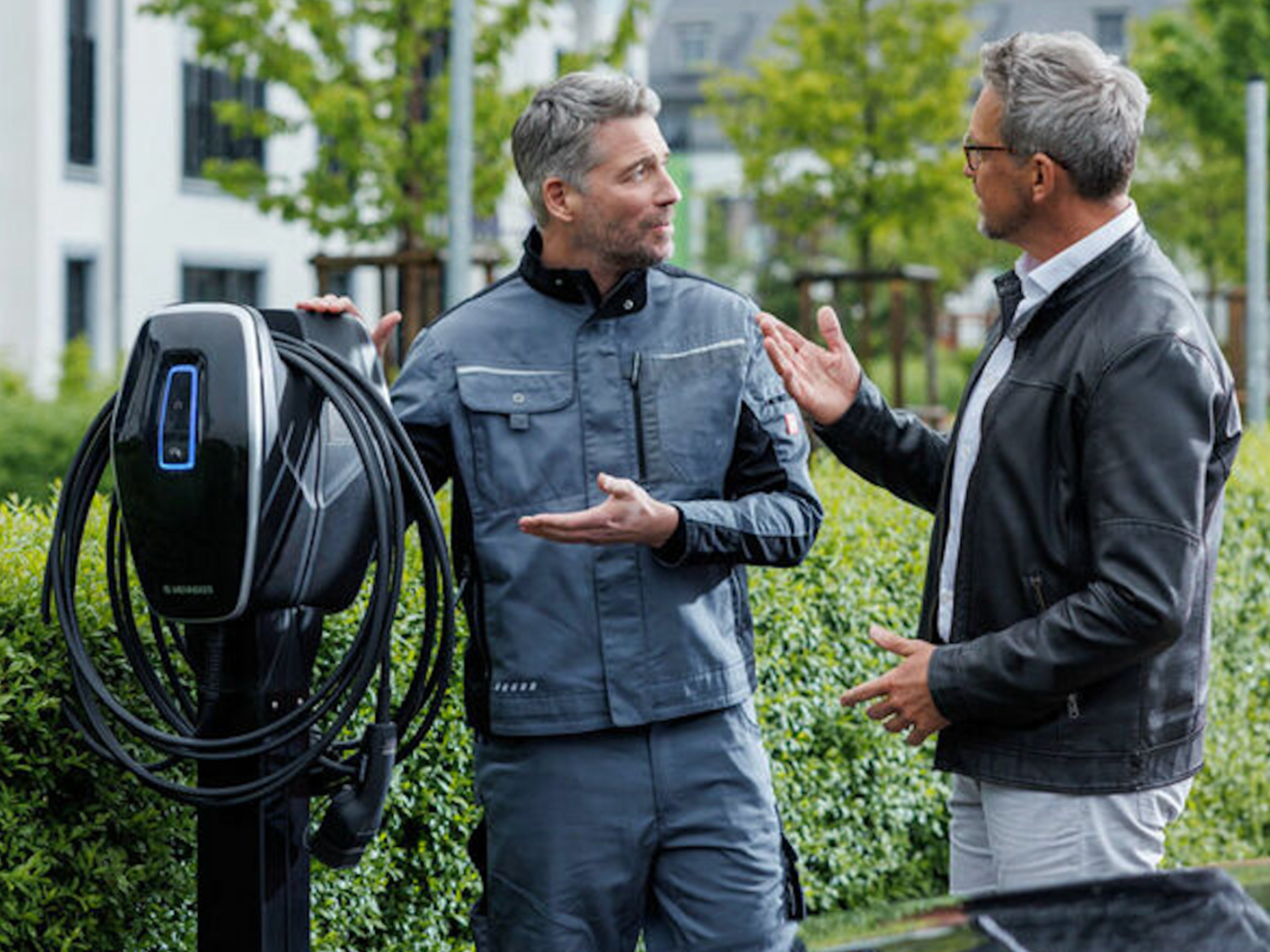 Zwei Männer stehen neben einer Wallbox und unterhalten sich.