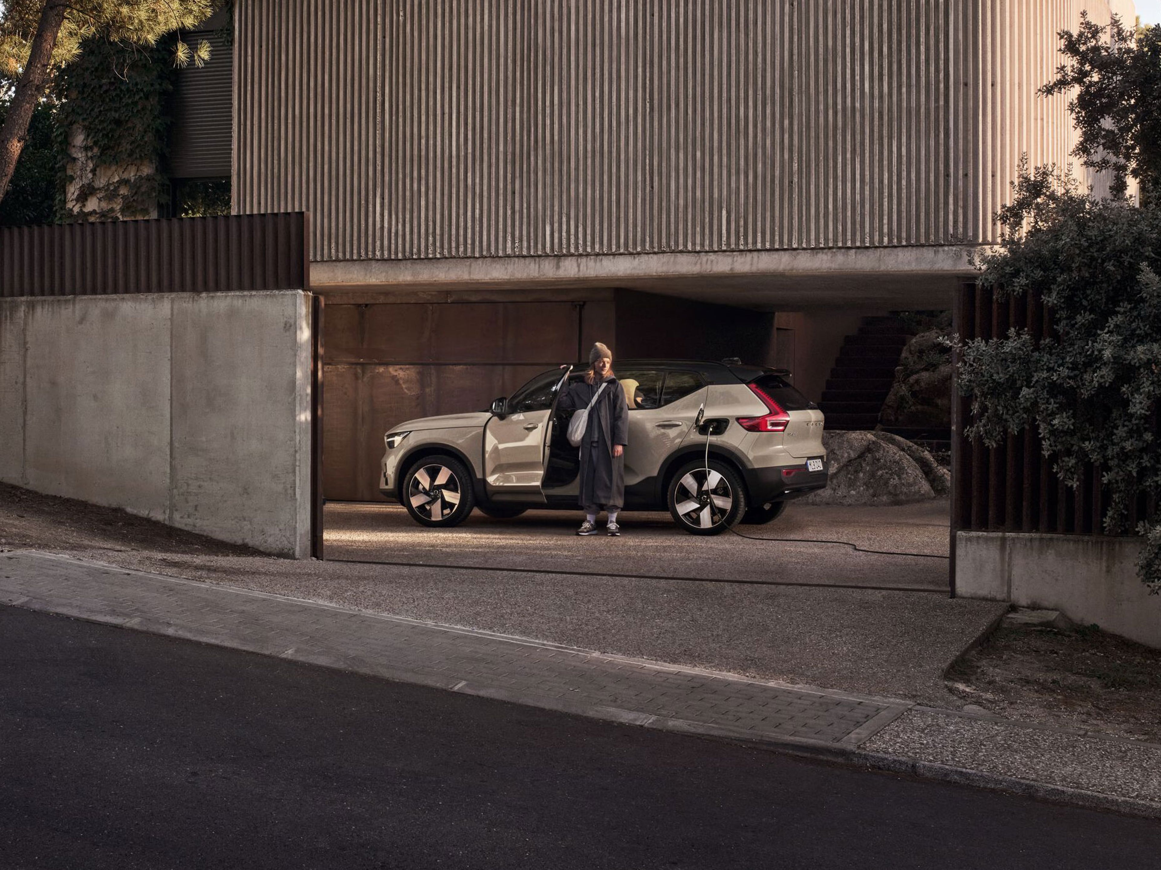 Femme debout près d’un EX40 Sable Dune devant une maison moderne entourée de végétation.