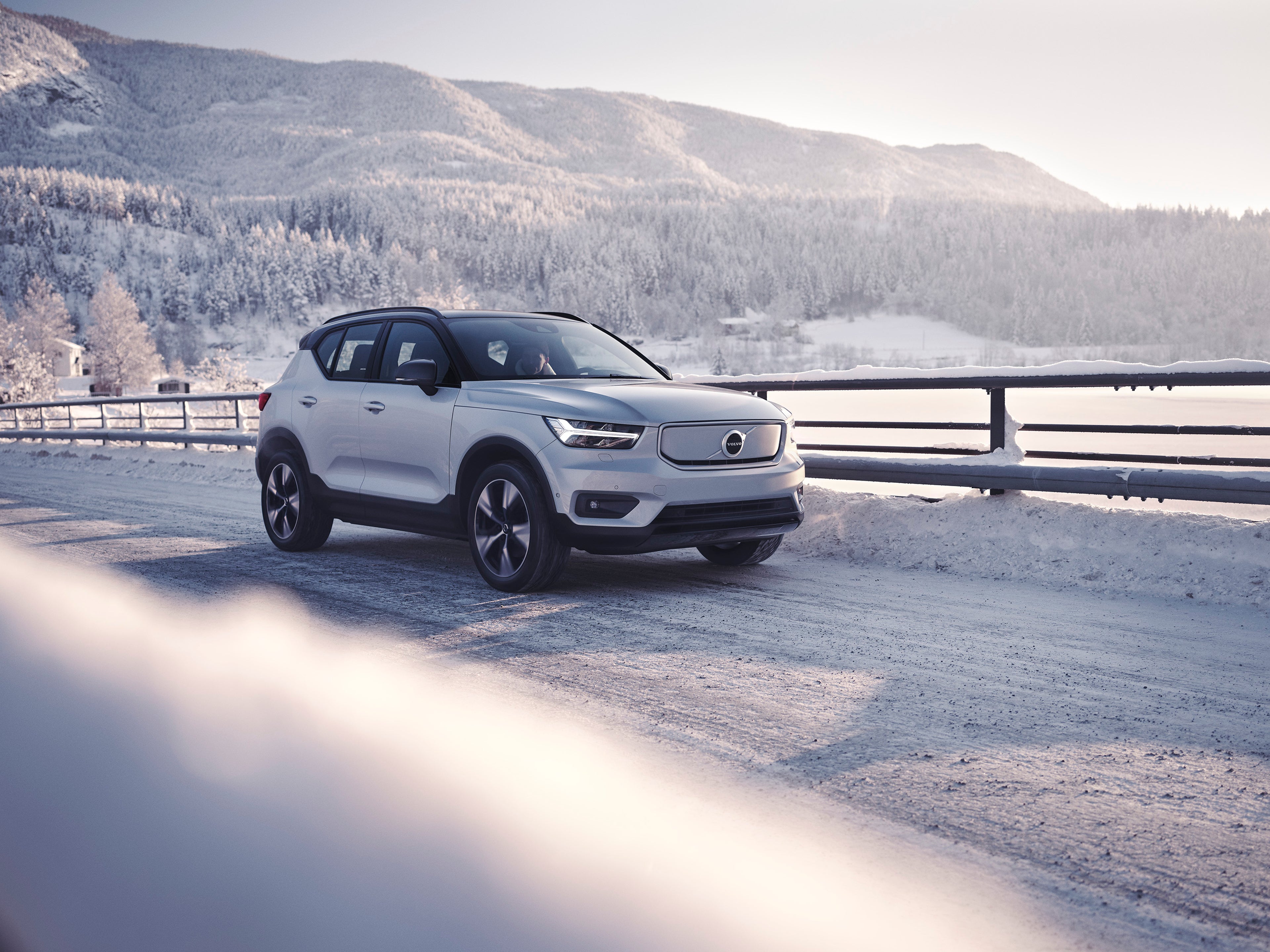A pure electric Volvo XC40 Recharge SUV driving across a snowy Scandinavian landscape.