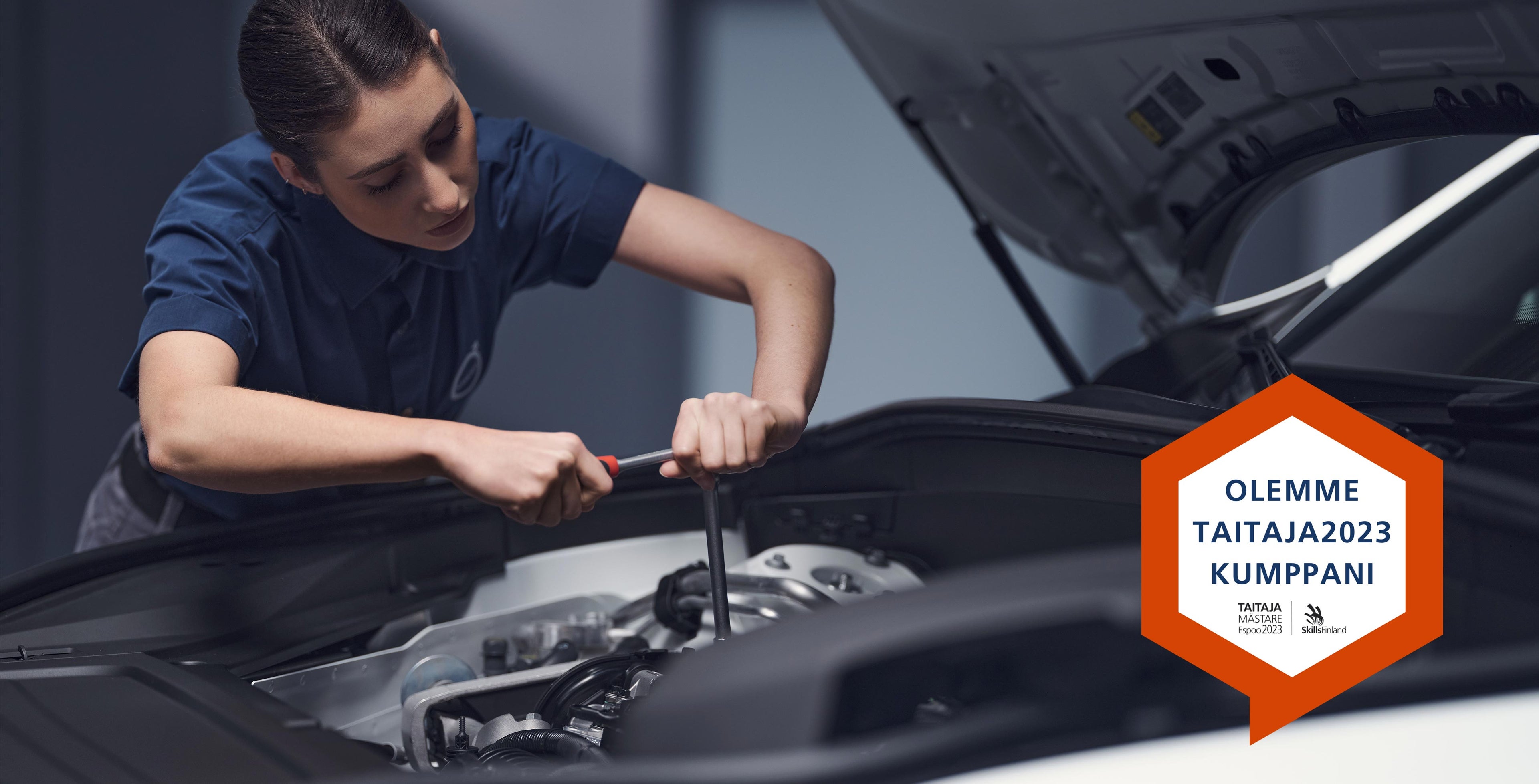 Volvo omamekaanikko nainen huoltaa autoa, kuvaan liitetty Taitaja 2023 kilpailun logo.