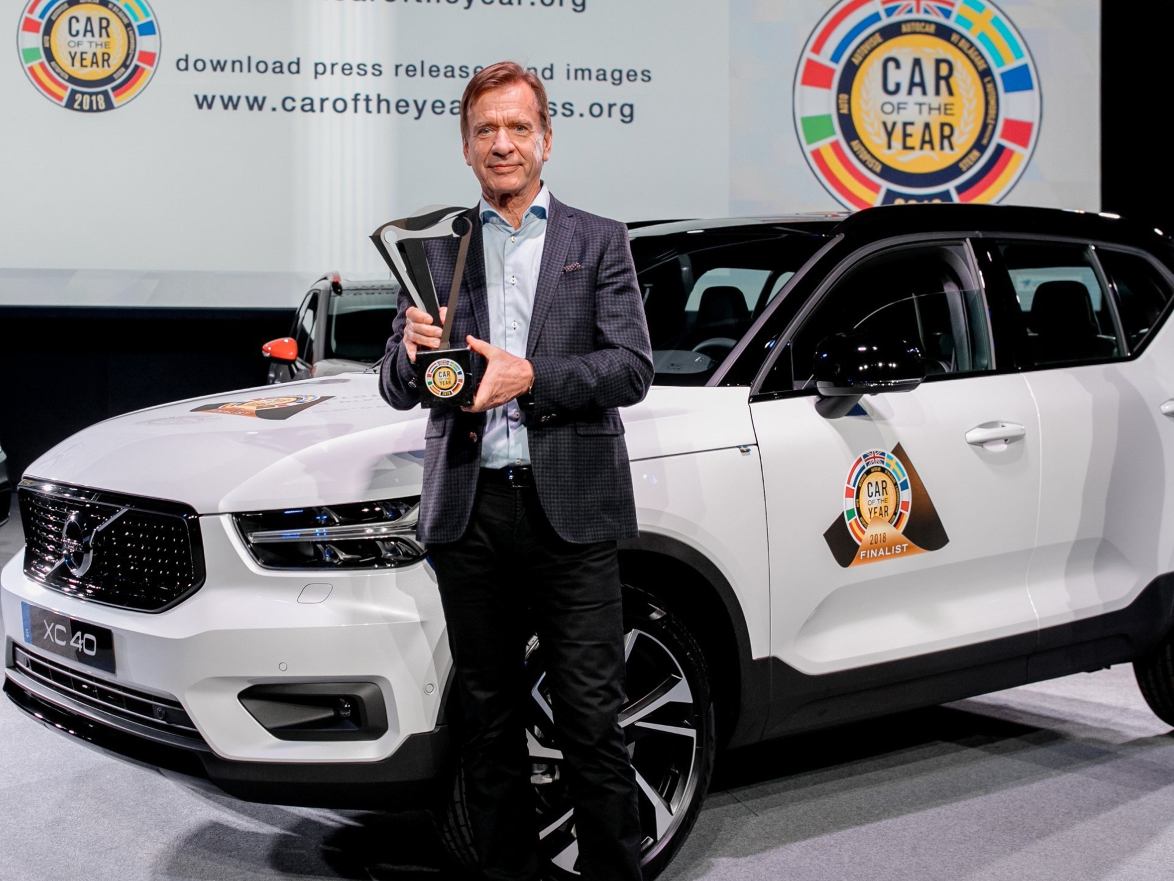 Der ehemalige Volvo Chef Hakan Samuelsson steht vor einem weissen Volvo XC40 mit schwarzem Dach und präsentiert den "Auto des Jahres" Award.