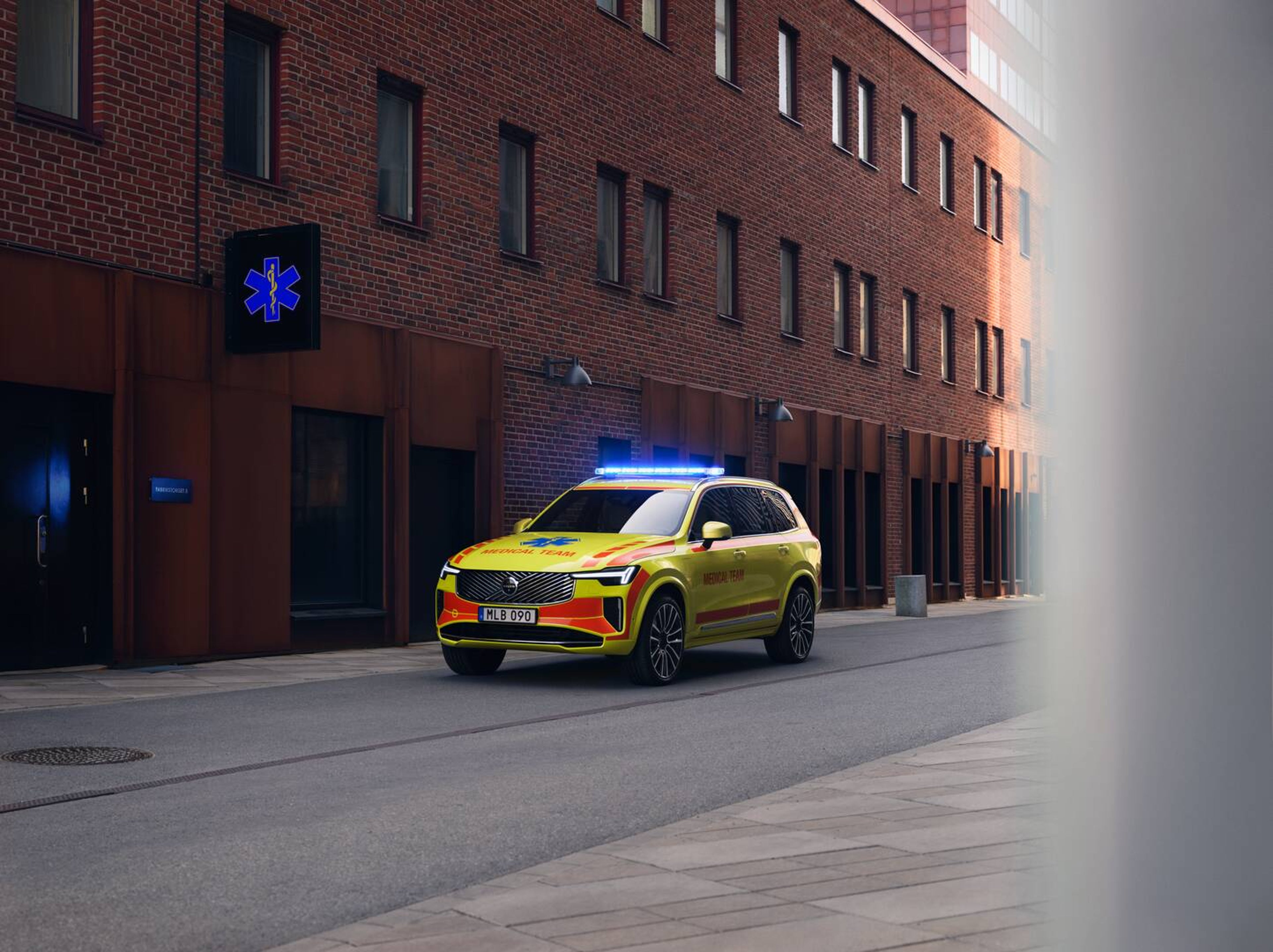 Egy sárga Volvo XC90 orvosi sürgősségi jármű parkol egy téglaépület előtt.
