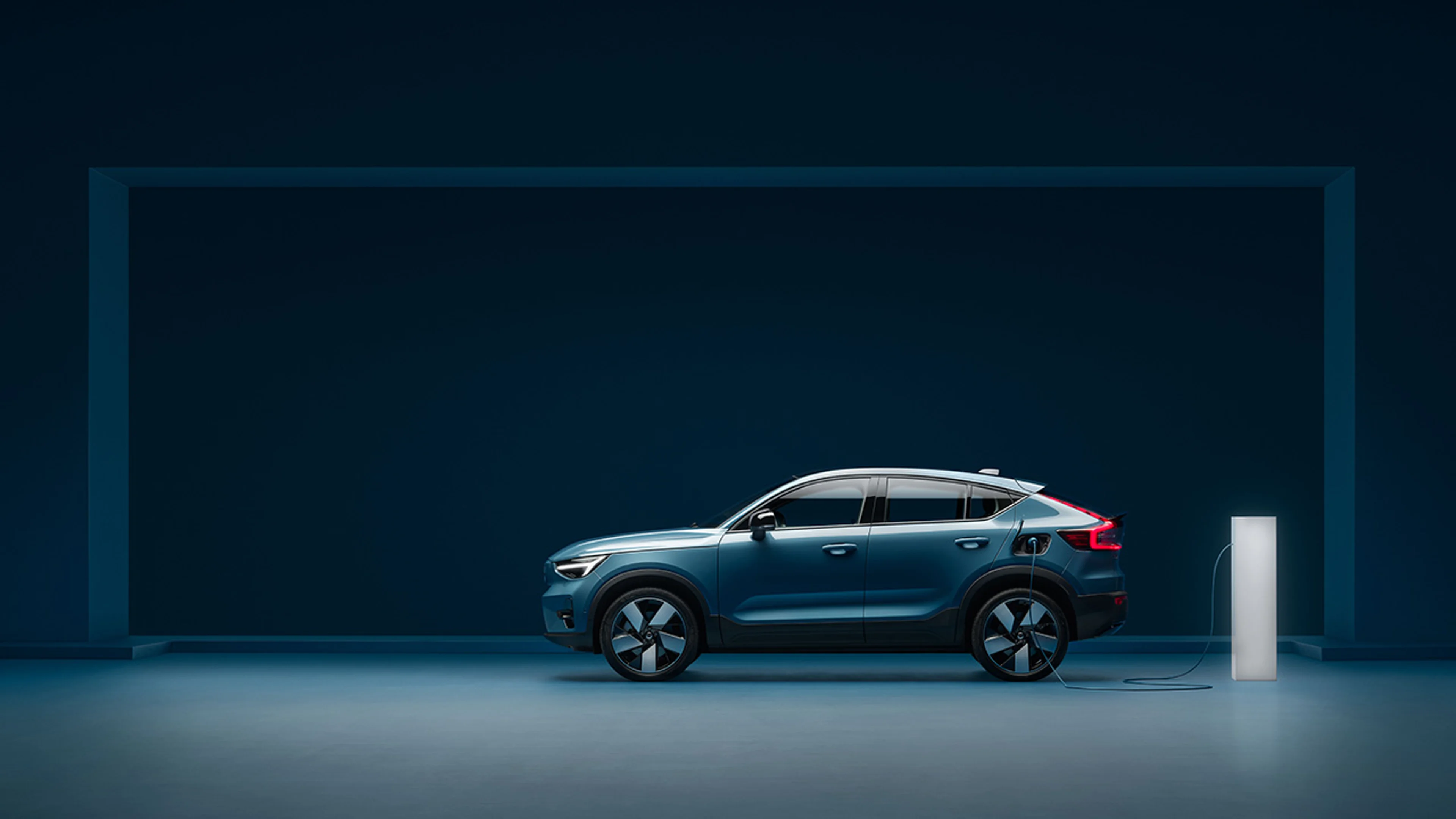 Volvo C40 Recharge in zijaanzicht naast een witte laadpaal in een blauwe studio-omgeving.