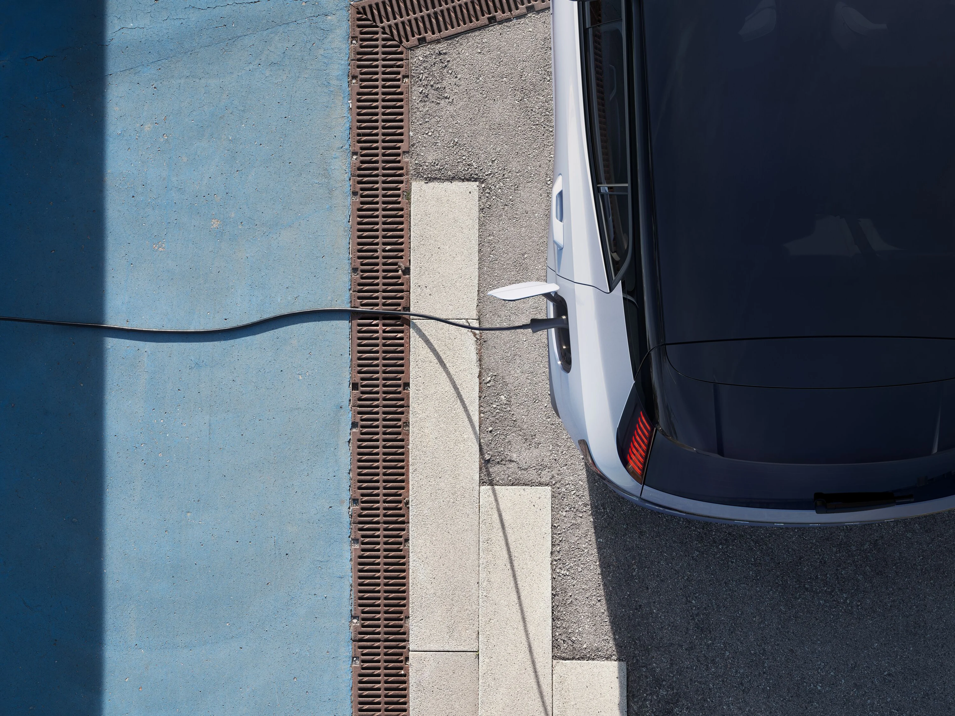Pohľad zhora na nabíjajúce sa elektrické vozidlo Volvo EX30 zaparkované na asfaltovom povrchu pri nabíjacej stanici.