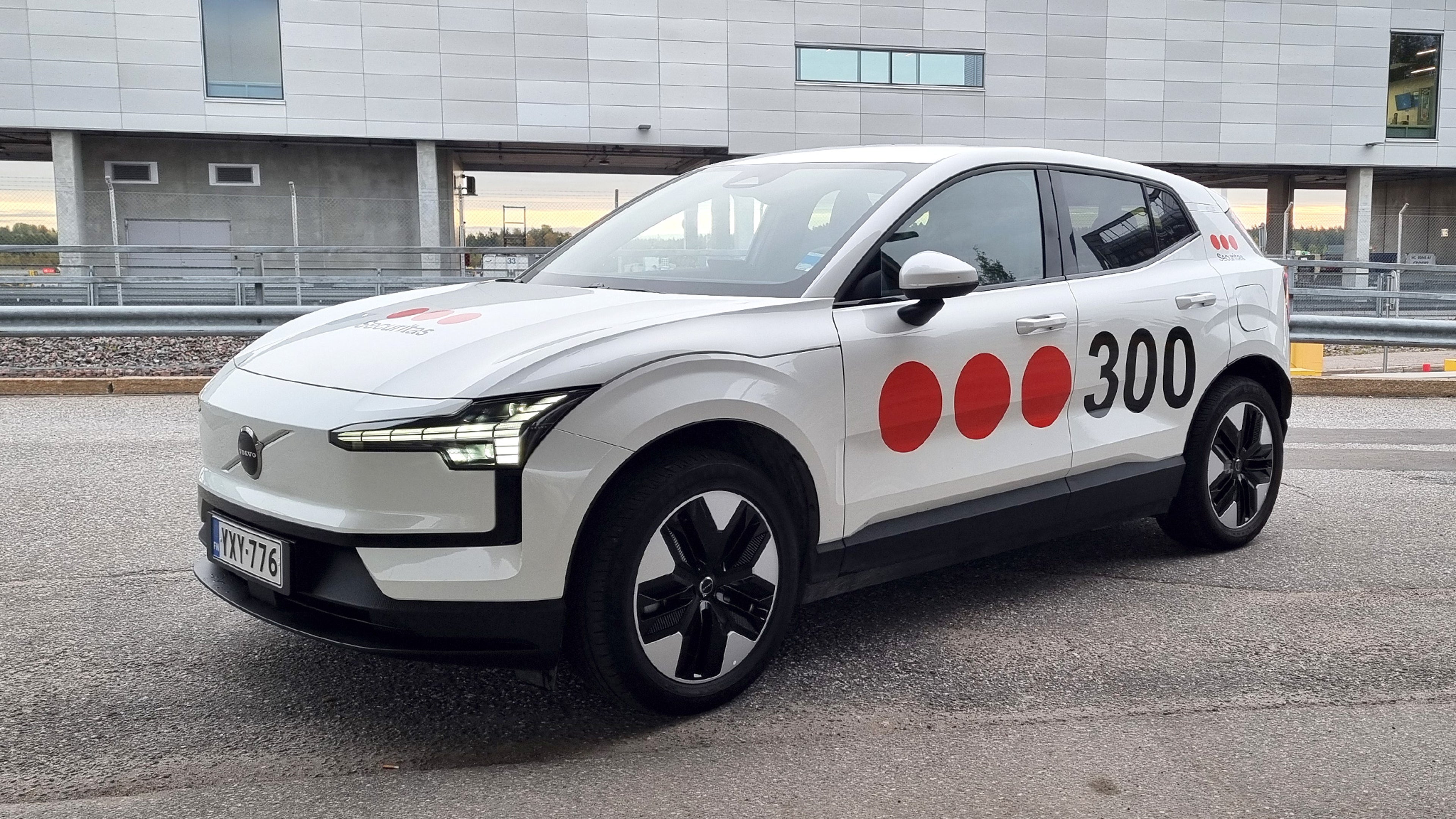 Securitaksen tunnuksin teipattu valkoinen Volvo EX30 täyssähköauto pysäköitynä parkkihalliin.