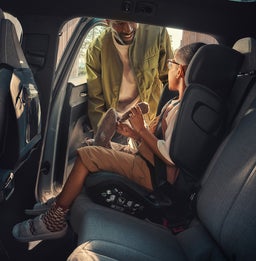 Een vader maakt zijn kind voorzichtig vast in een kinderzitje in een Volvo, zodat het goed zit. Het interieur benadrukt Volvo's focus op kindveiligheid.