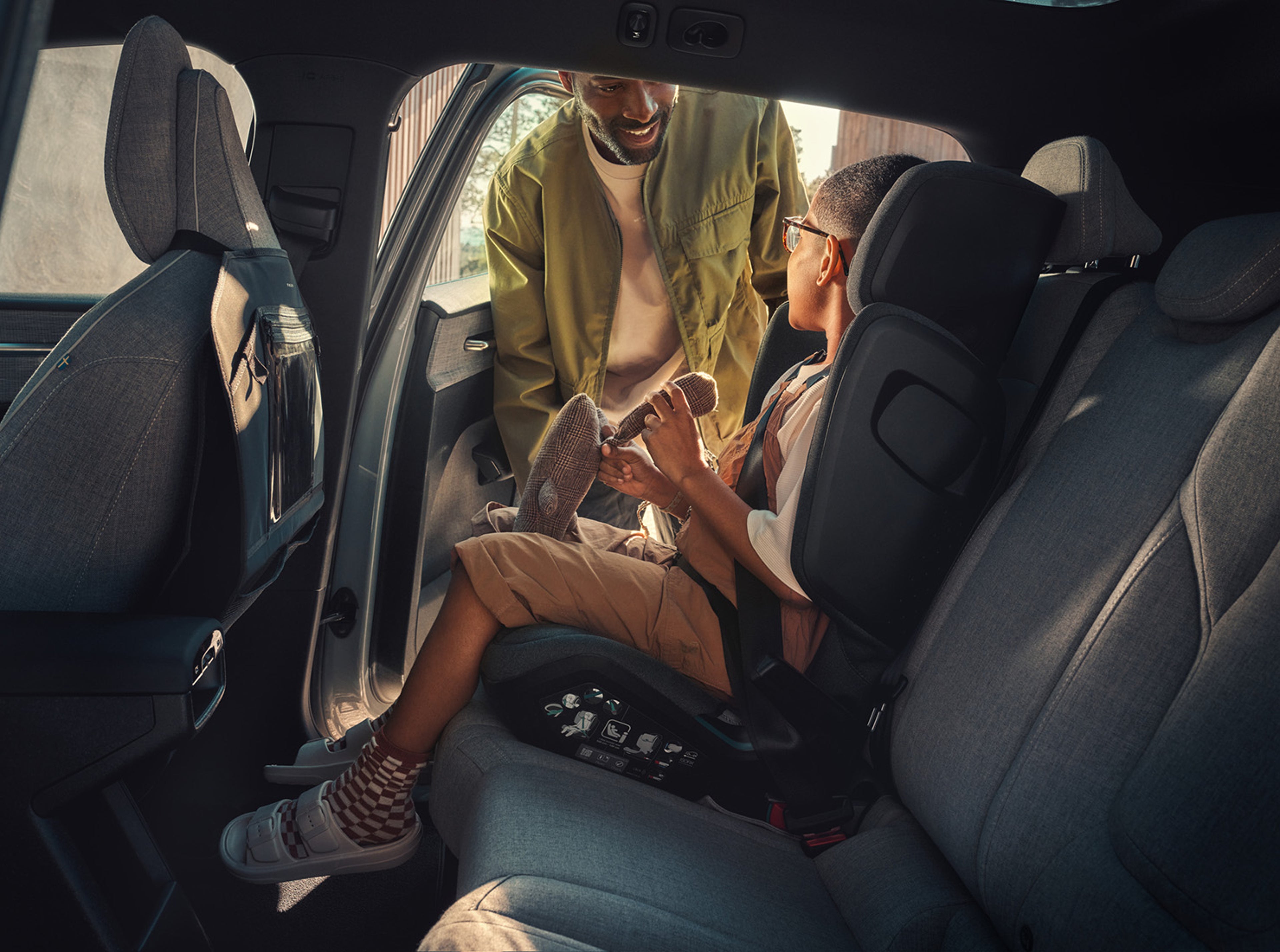 Een vader maakt zijn kind voorzichtig vast in een kinderzitje in een Volvo, zodat het goed zit. Het interieur benadrukt Volvo's focus op kindveiligheid.