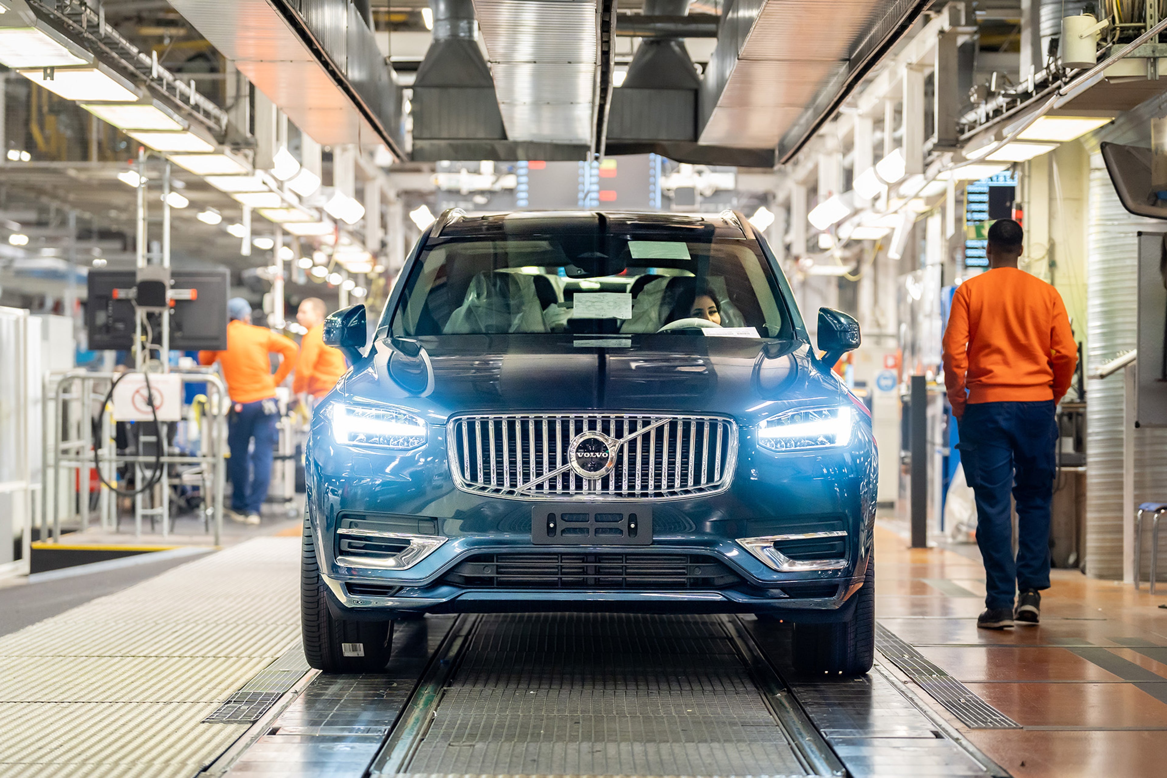A female sits on the driver seat of a blue Volvo Car at the production line.