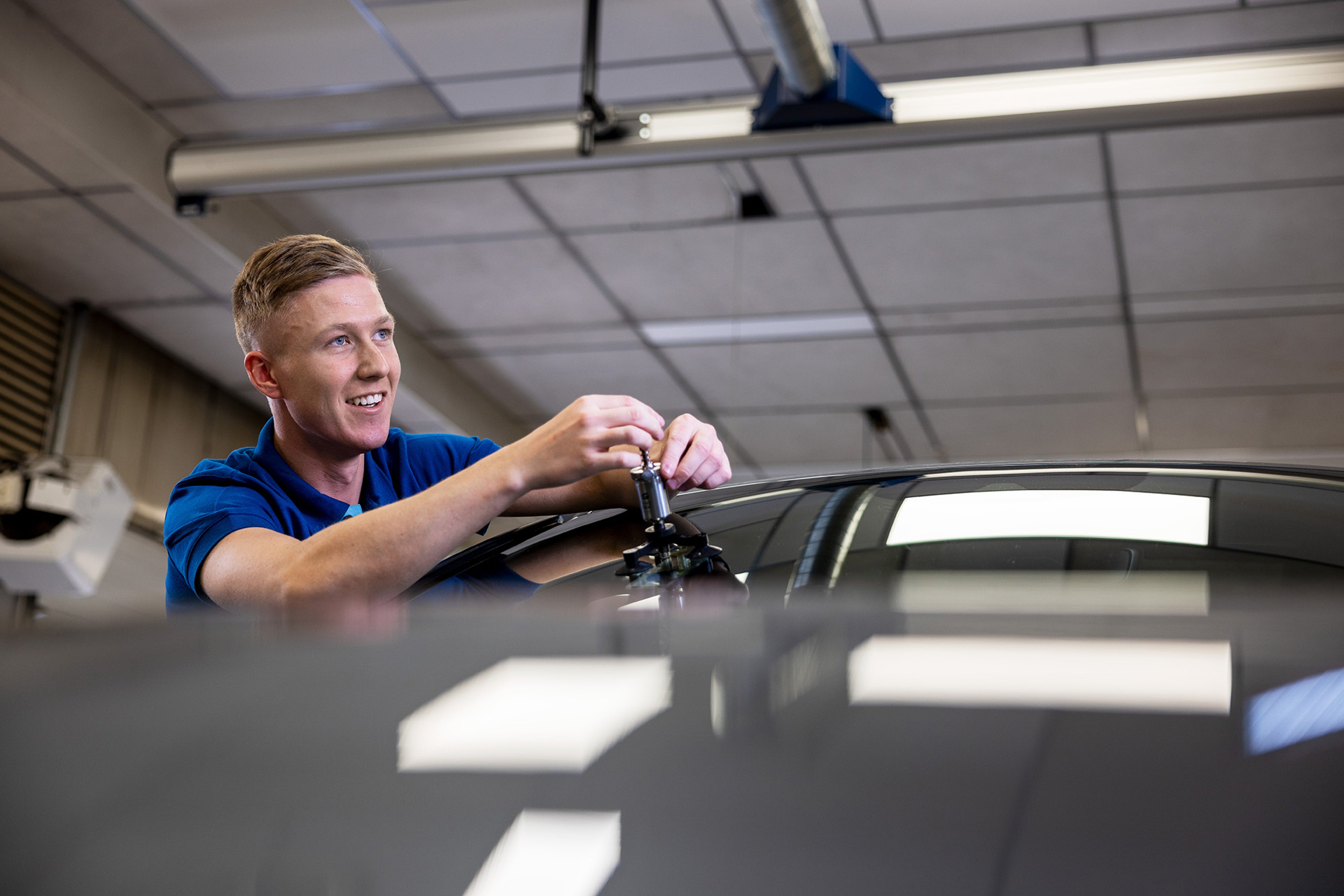En smilende Volvo Cars sertifisert servicetekniker som fikser frontruten på en Volvo