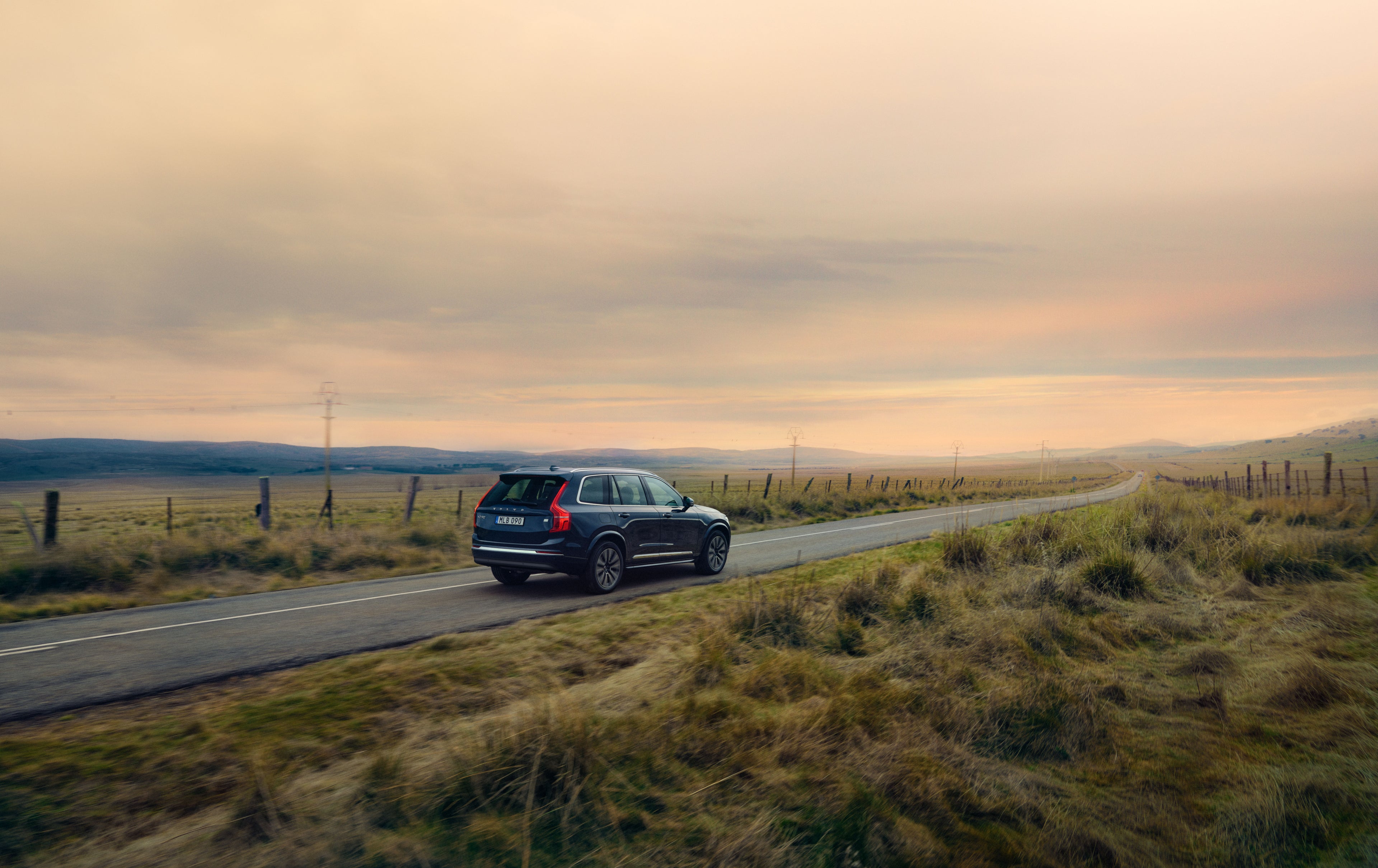 A Volvo XC90 driving on country road with fence on both sides