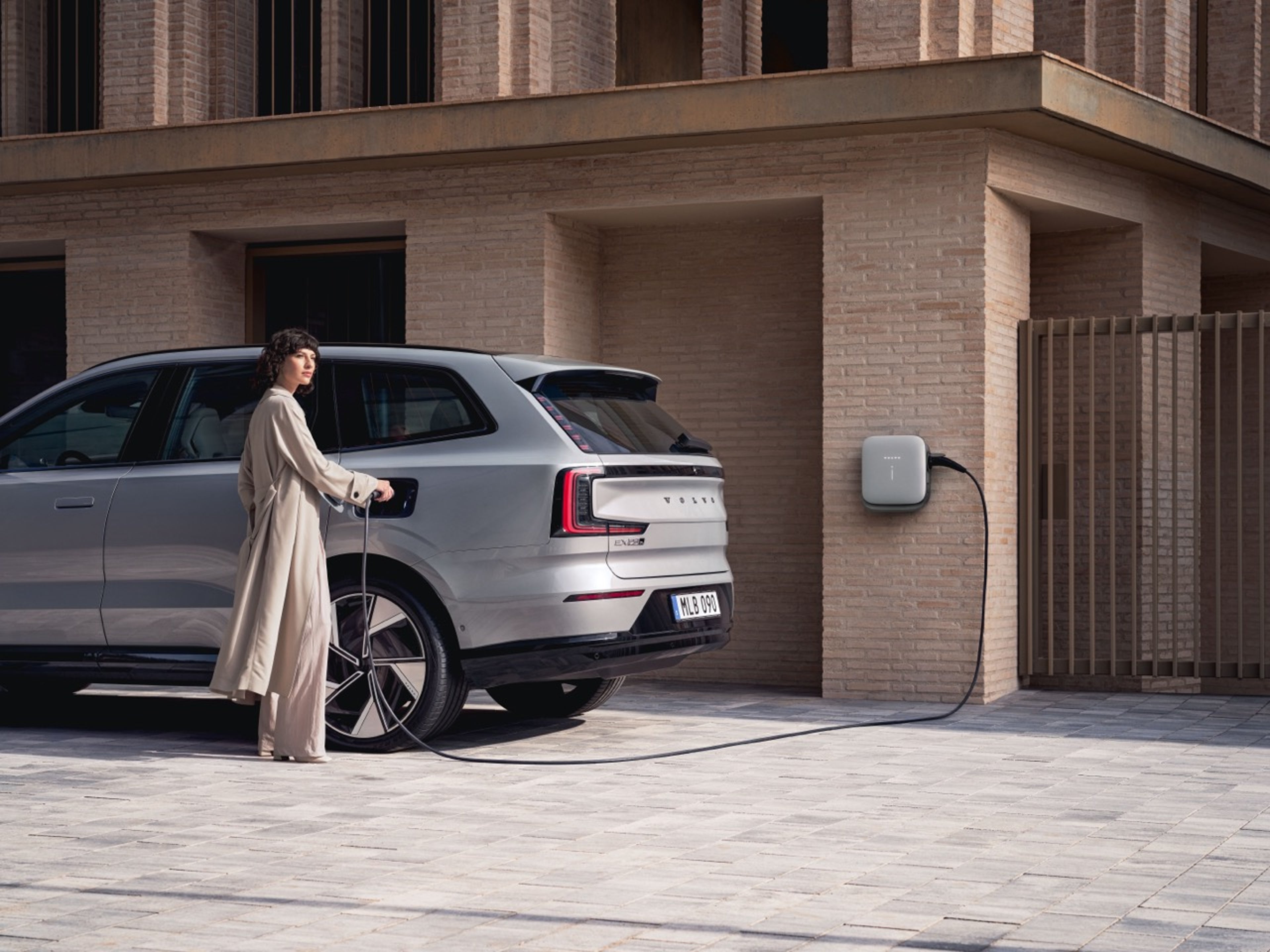 Moteris prie savo „Volvo EX90“ automobilio prijungia įkrovimo laidą.