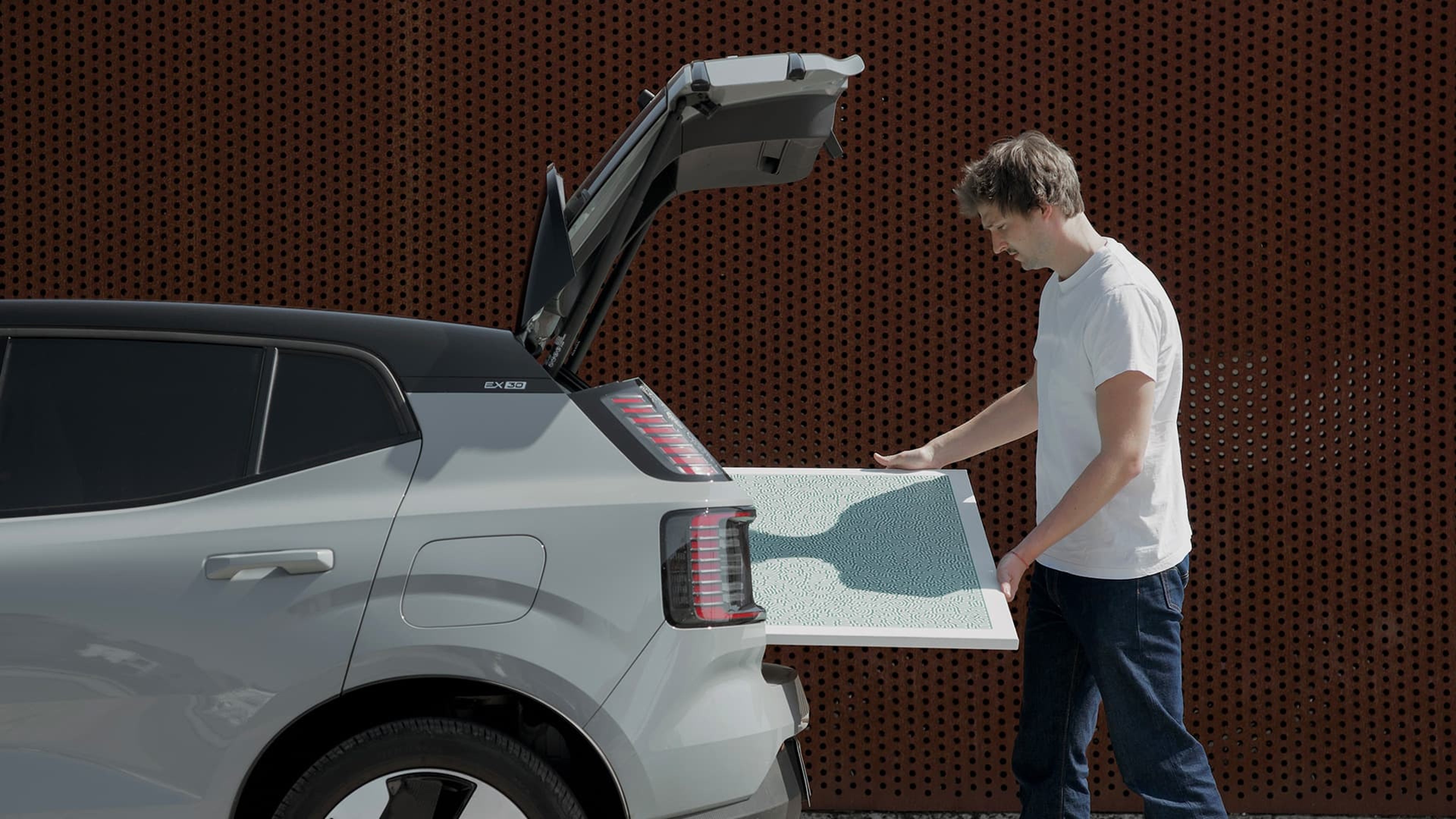 Jules Wittock se tient près du hayon ouvert d'une EX30 grise et charge un objet dans le coffre.