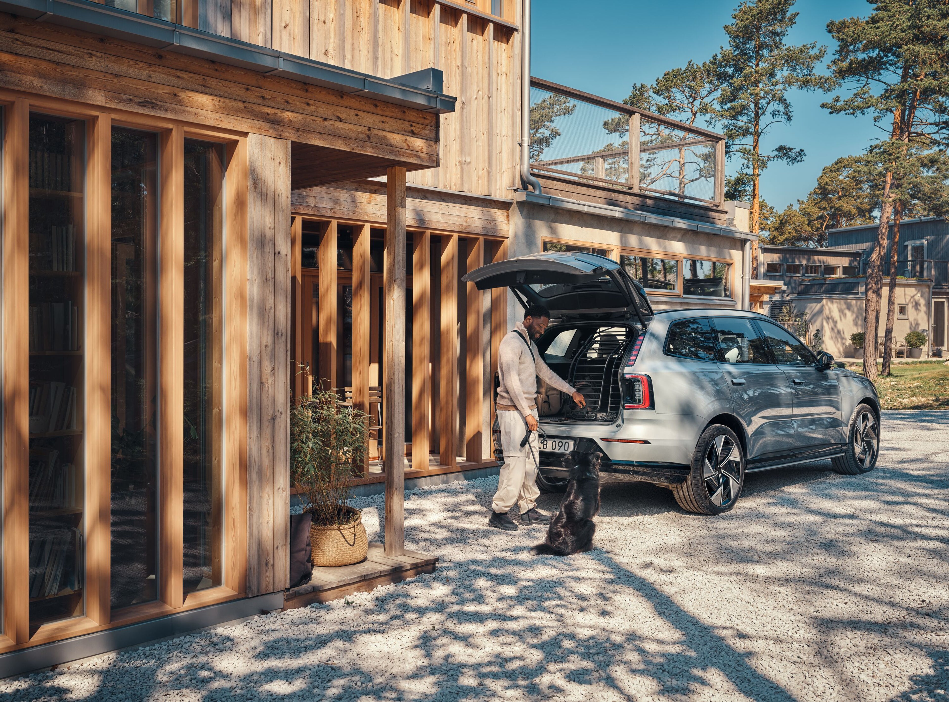 Saulėtą dieną prie namų vyras ragina šunį įšokti į automobilio bagažinę.