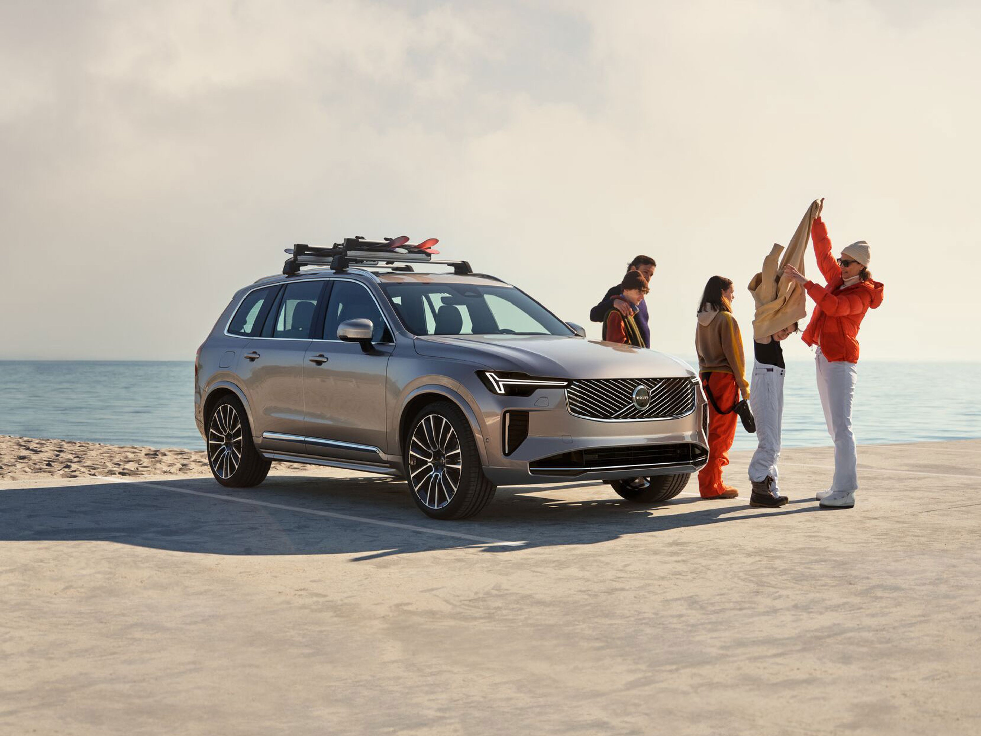 XC90 Argent Crépuscule garé dans un parking en bord de mer avec une famille de quatre personnes debout à côté