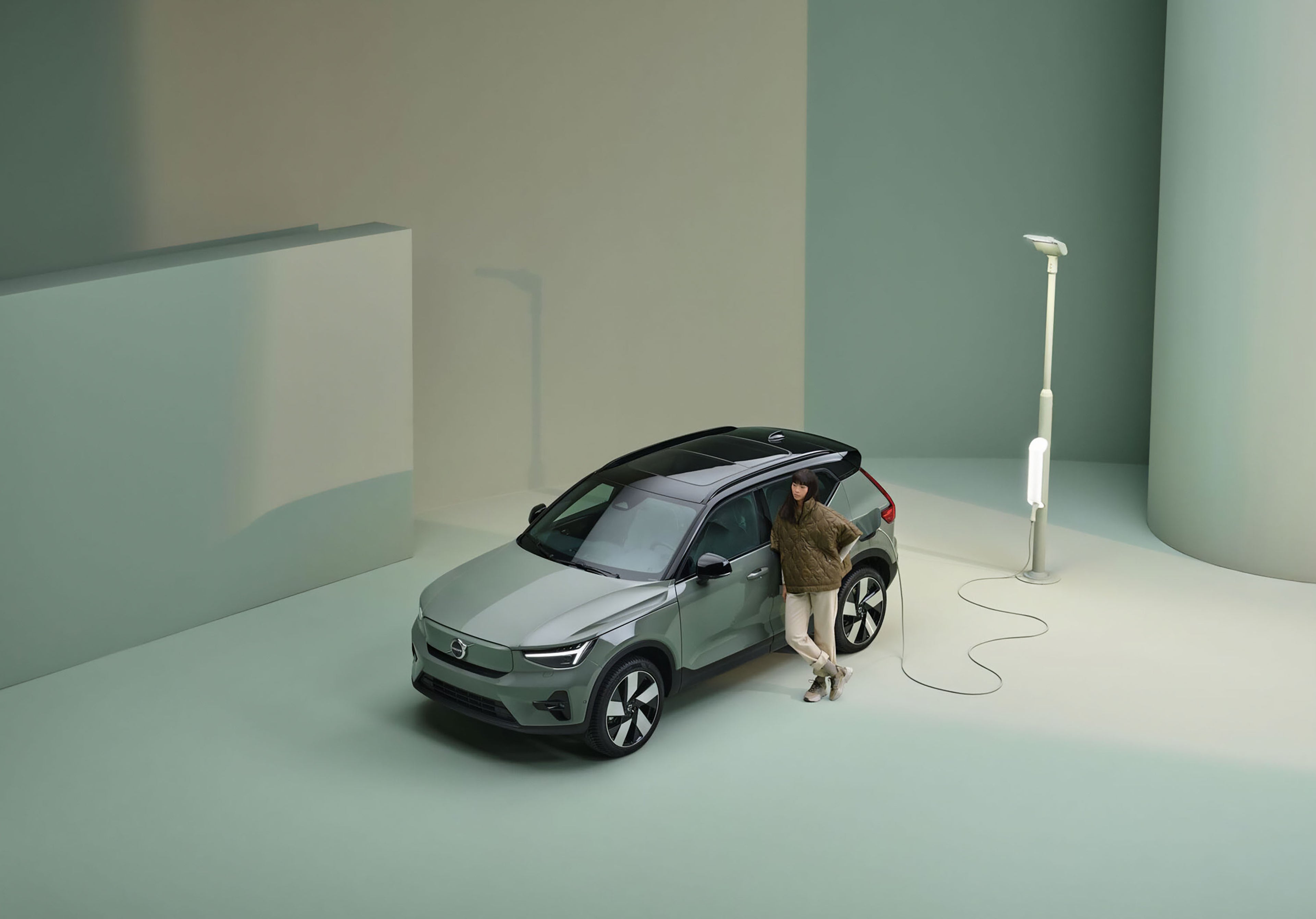 žena opretá o stojace auto pripojené k nabíjaniu