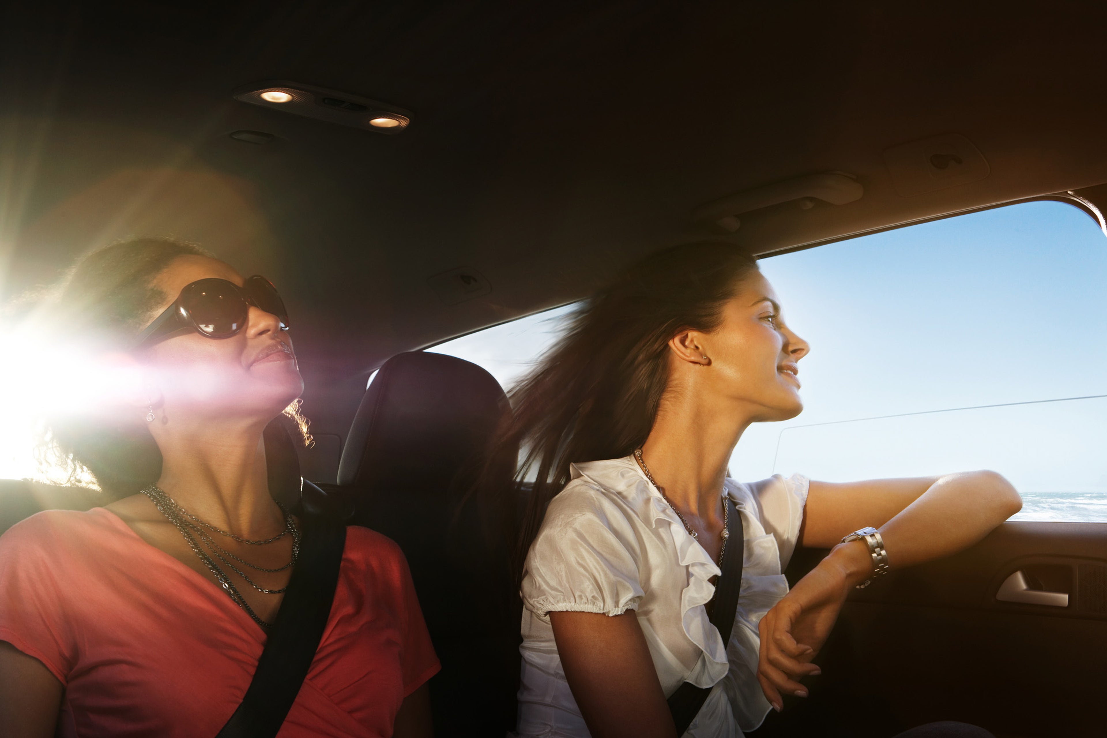 Two women in a car, wearing seatbelts, enjoying the sunlight.