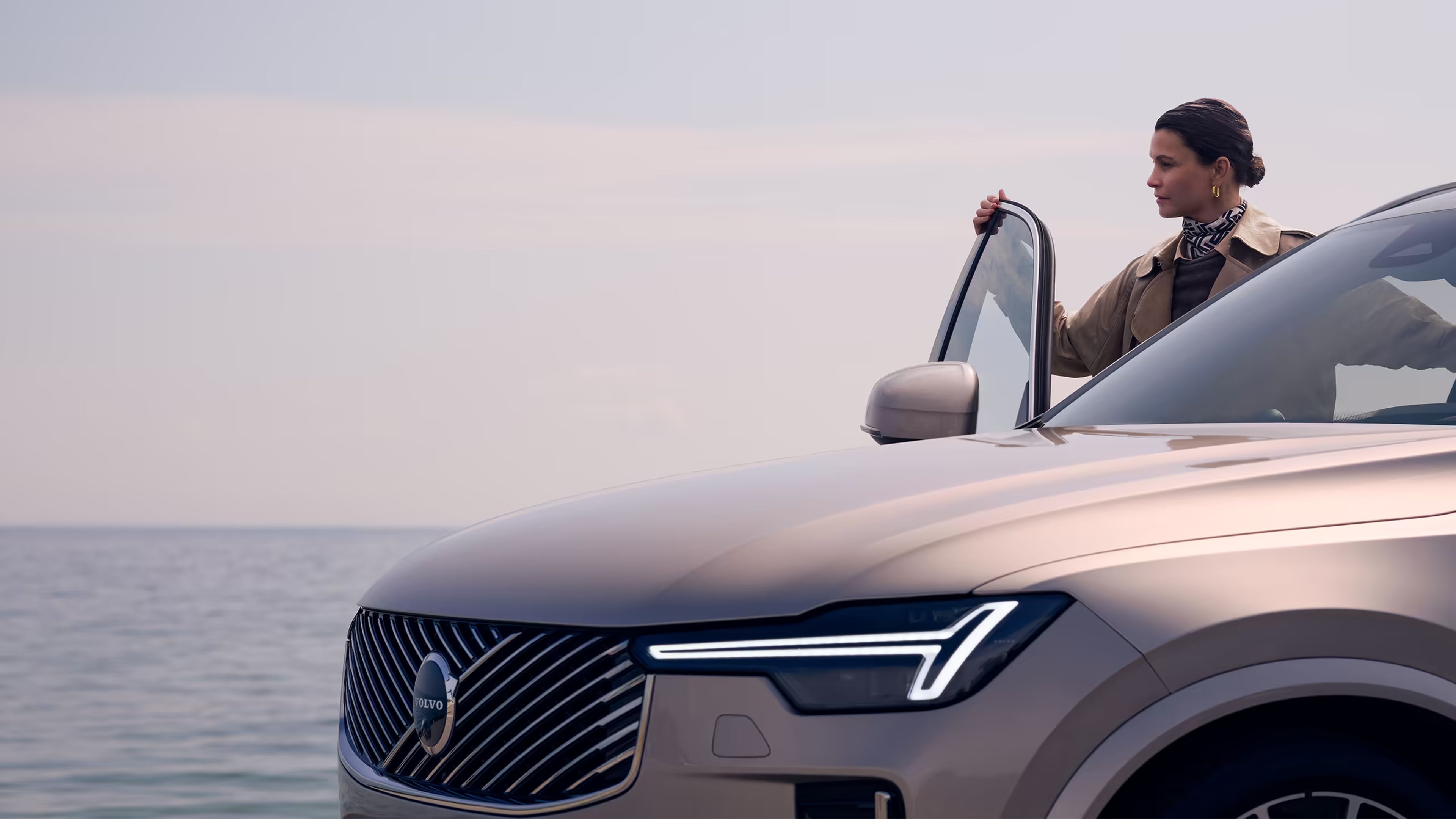 Una mujer sosteniendo abierta la puerta de un Volvo XC90, mirando hacia el océano