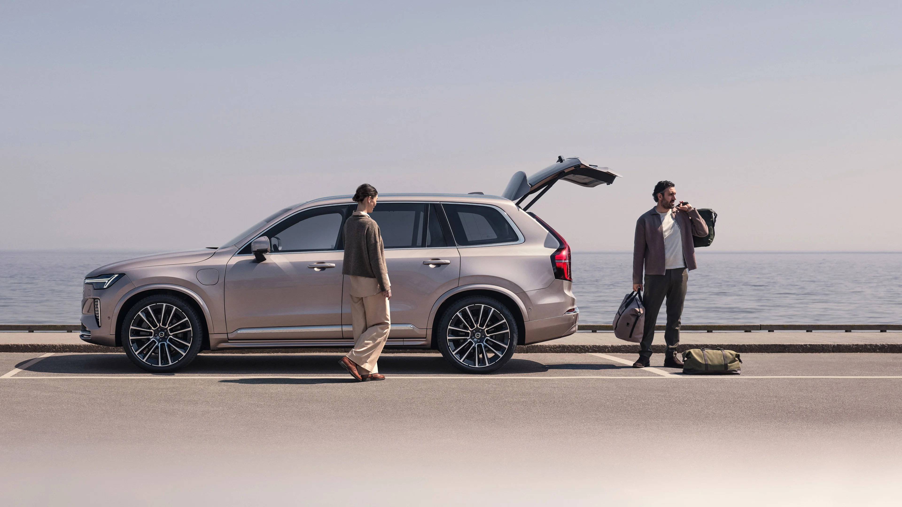 Ženska stoji ob Volvu XC90, moški zlaga stvari iz prtljažnika.