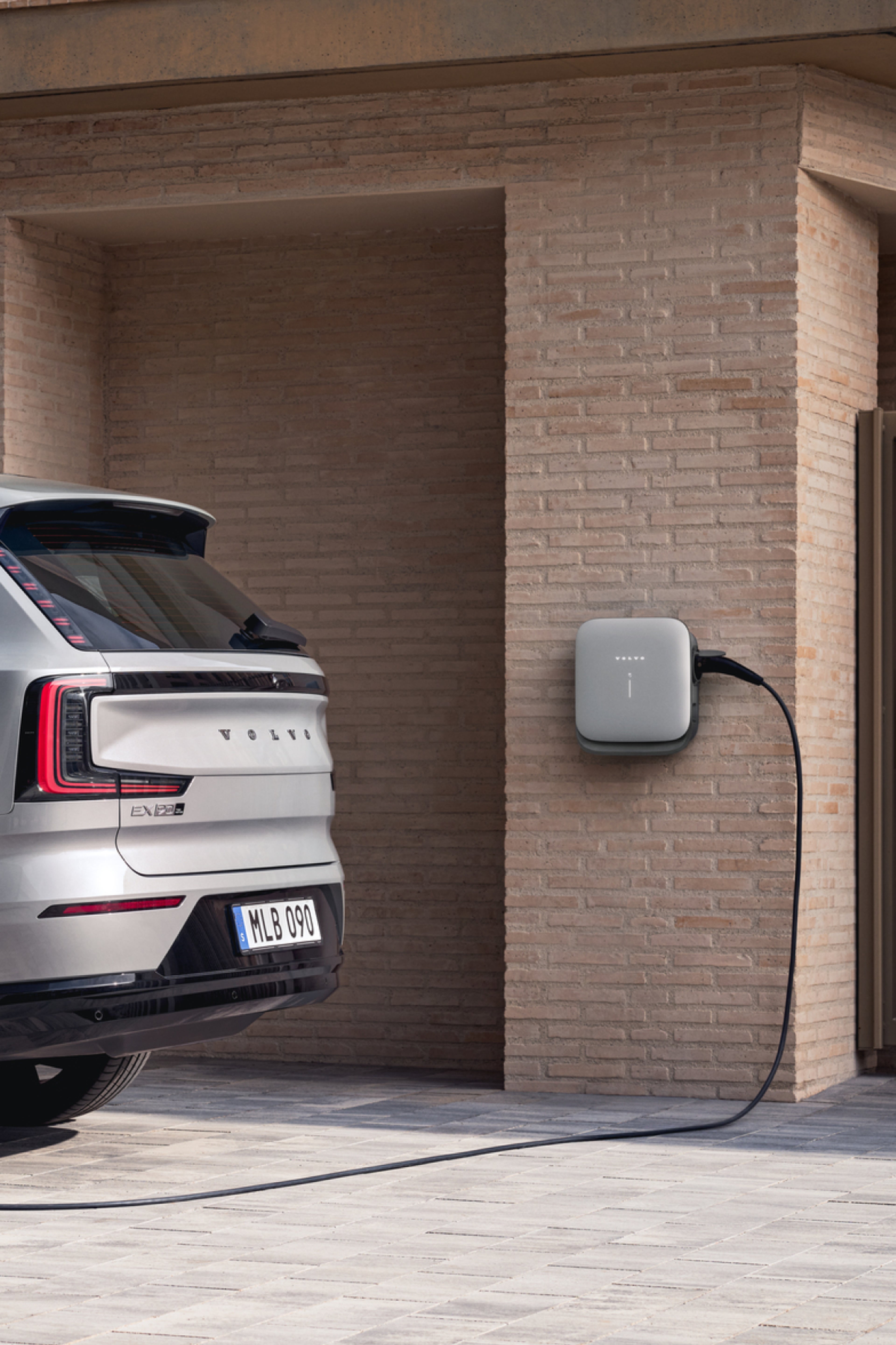 Moteris įkrauna savo „Volvo EX90“, prijungtą prie sieninės stotelės, pritvirtintos prie mūrinės sienos