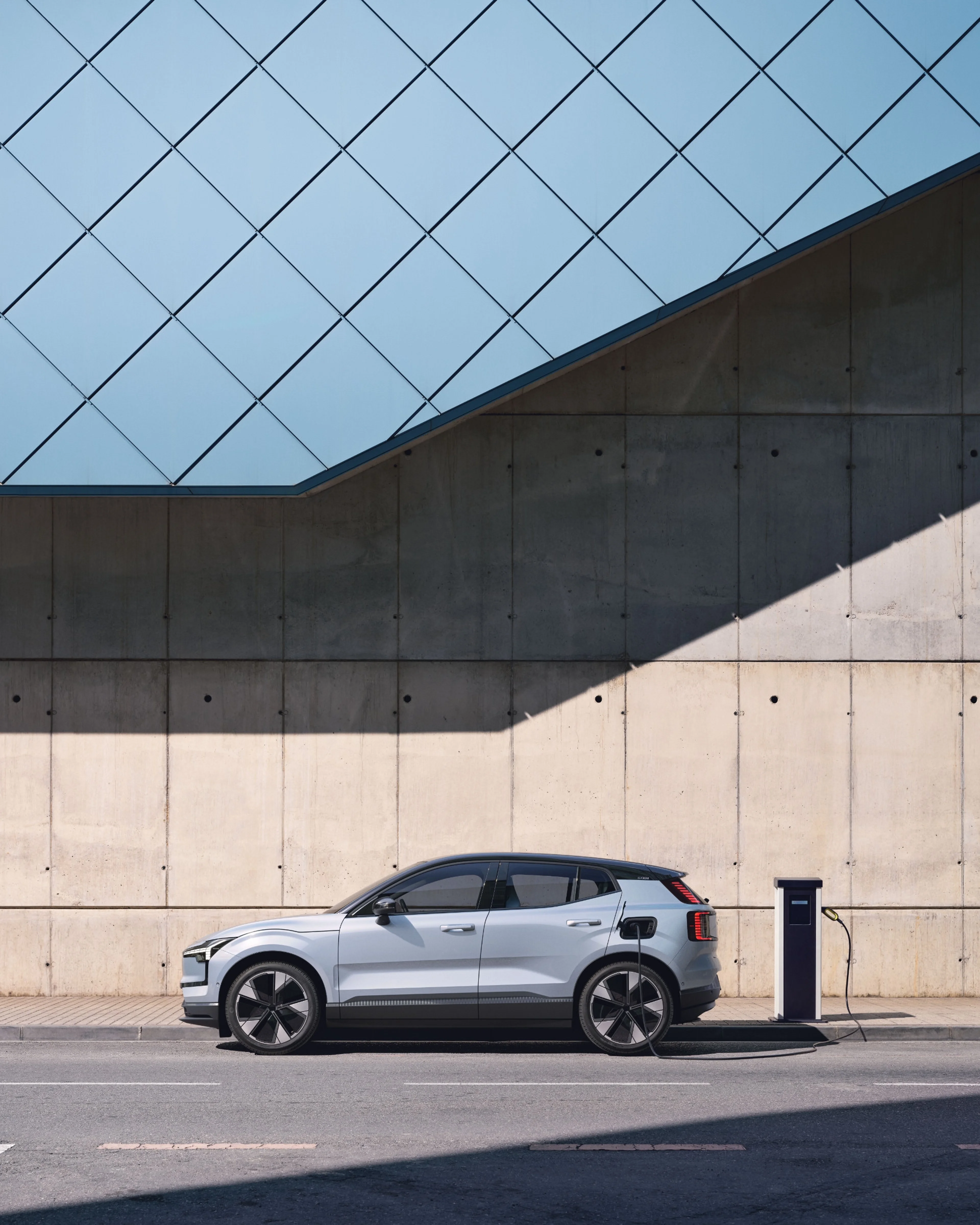 Ein Volvo EX30 in Cloud Blue steht vor einer beigen Wand und wird geladen.