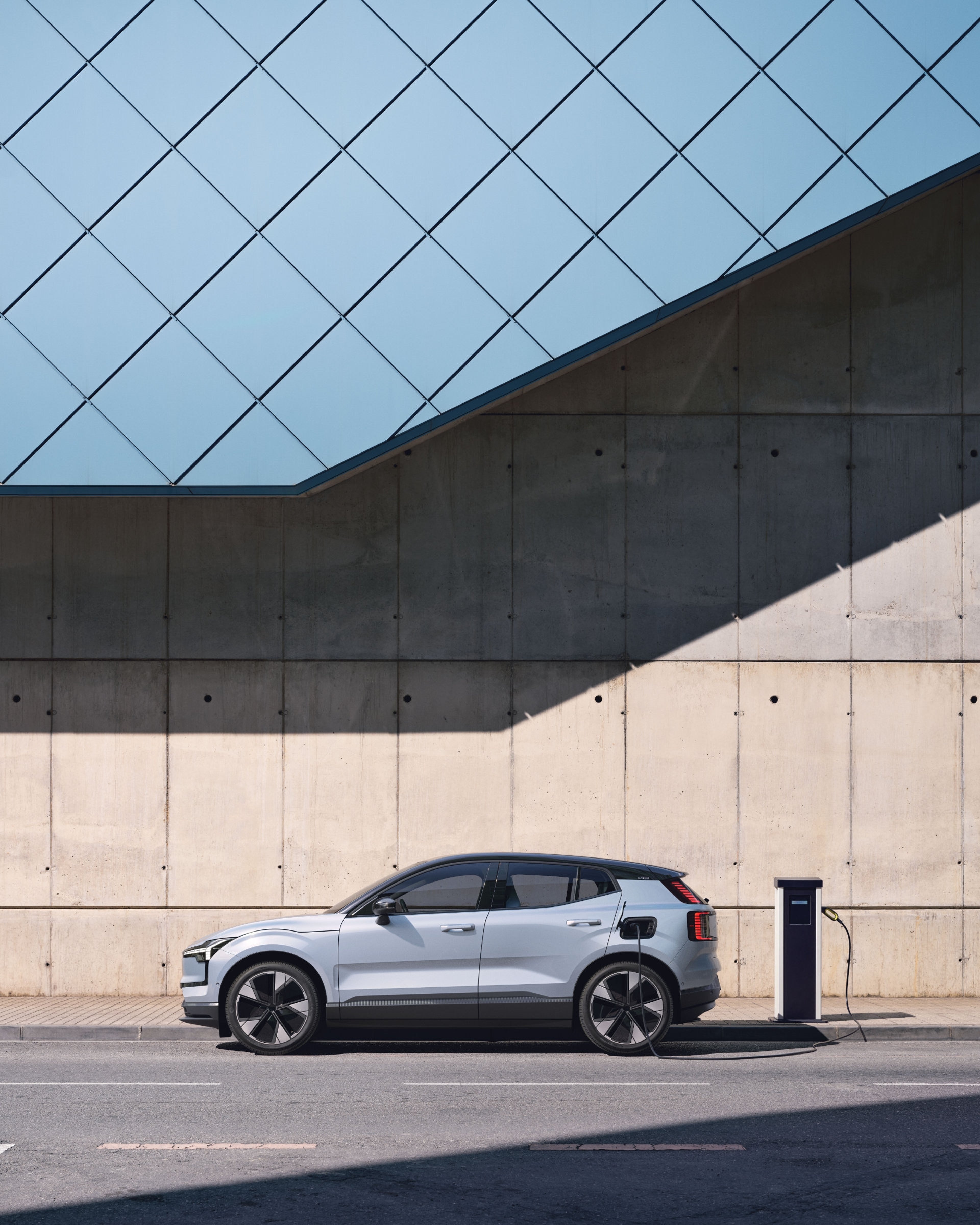 Ein Volvo EX30 in Cloud Blue steht vor einer beigen Wand und wird geladen.