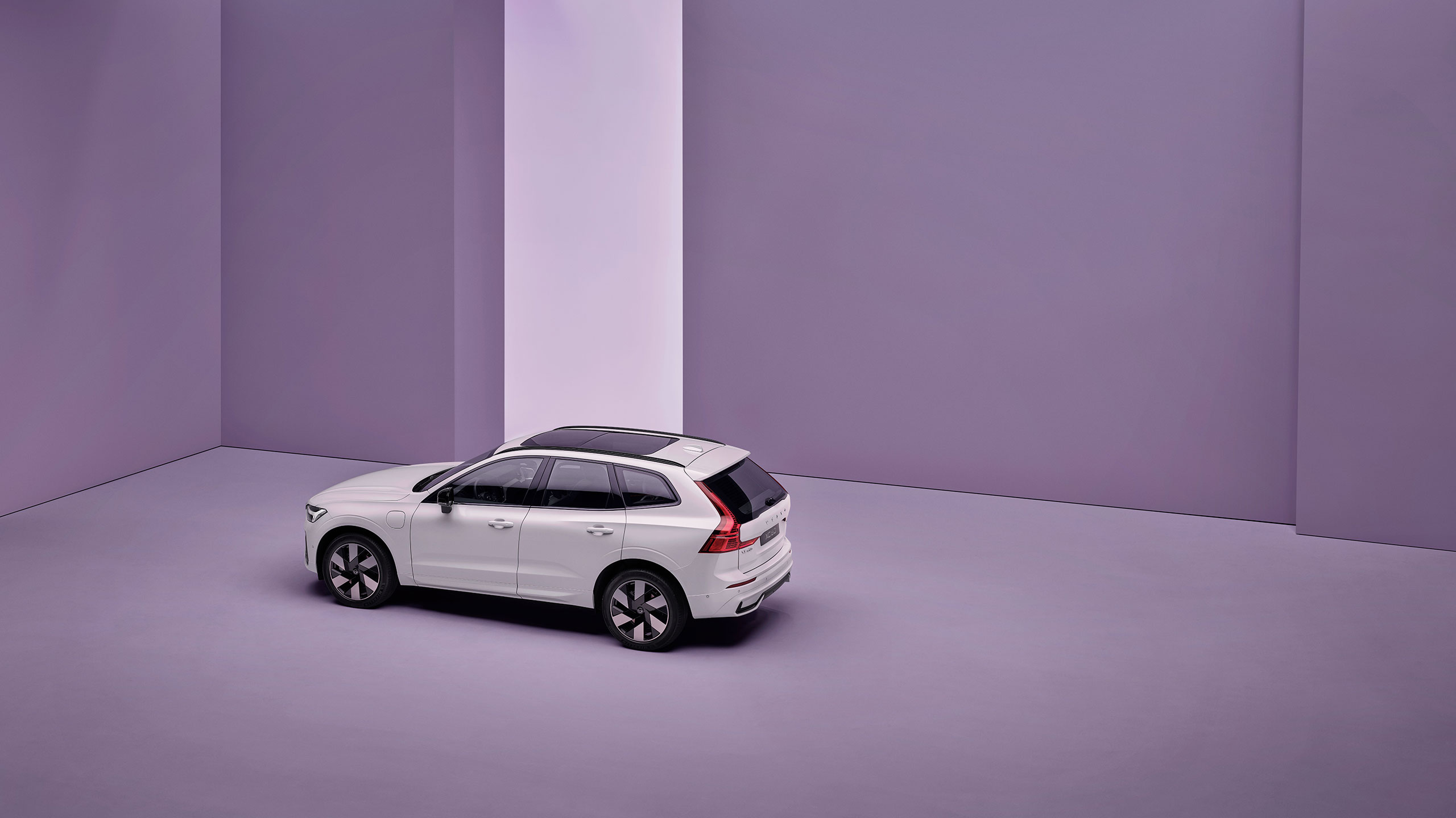 Long distance view of a parked Volvo XC60 plug-in hybrid car in an open, empty indoor space.