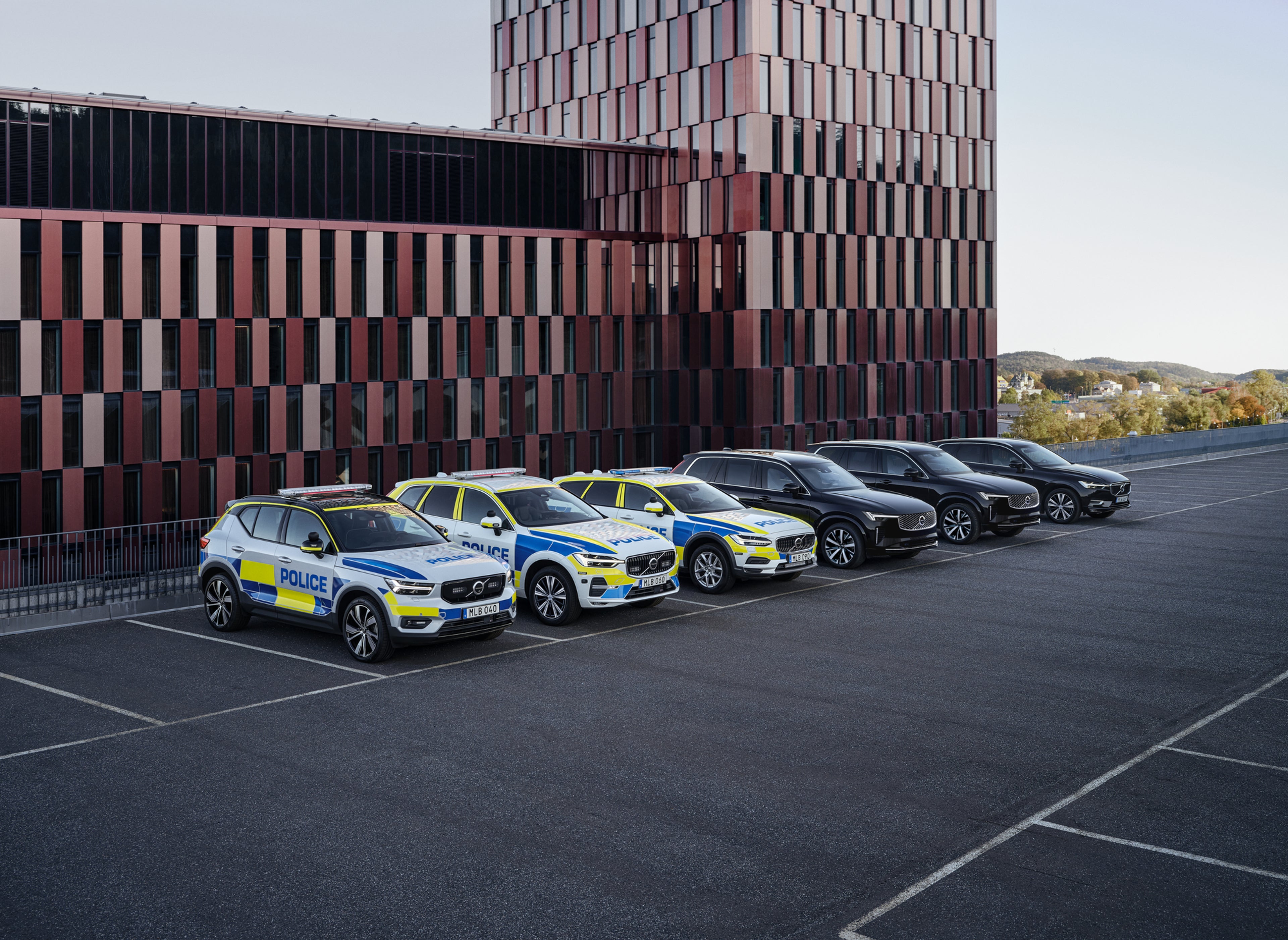 Tre Volvo-polisbilar och tre bepansrade Volvo-SUV:ar parkerade utanför en officiell byggnad.
