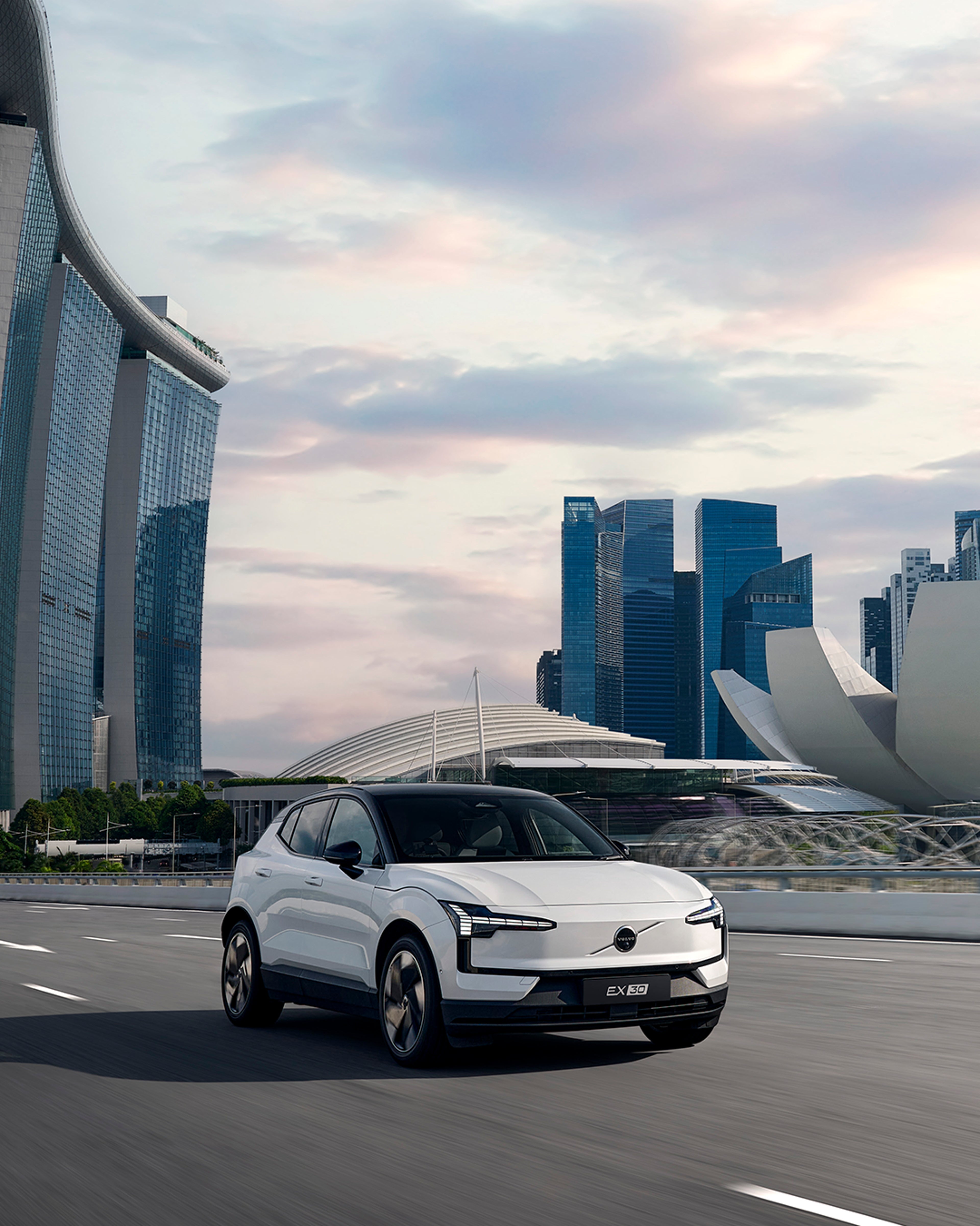 A Volvo EX30 sits parked turned away from the viewer, still and isolated in a surreal mountainous landscape.