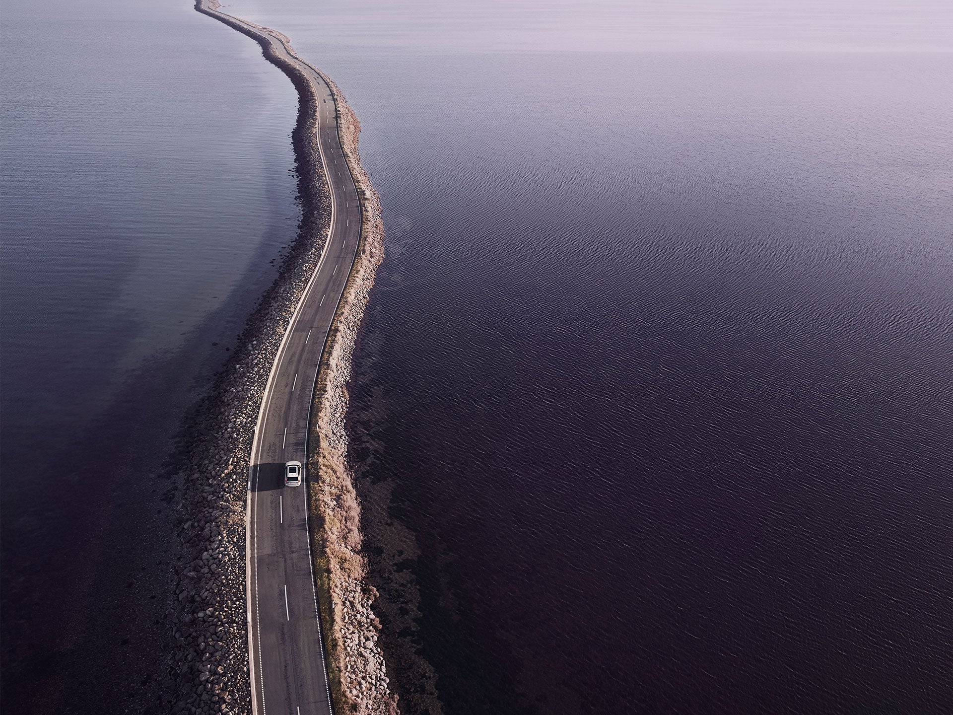 Una toma desde un ángulo alto de un SUV híbrido enchufable Volvo circulando en modo Power por una carretera costera.