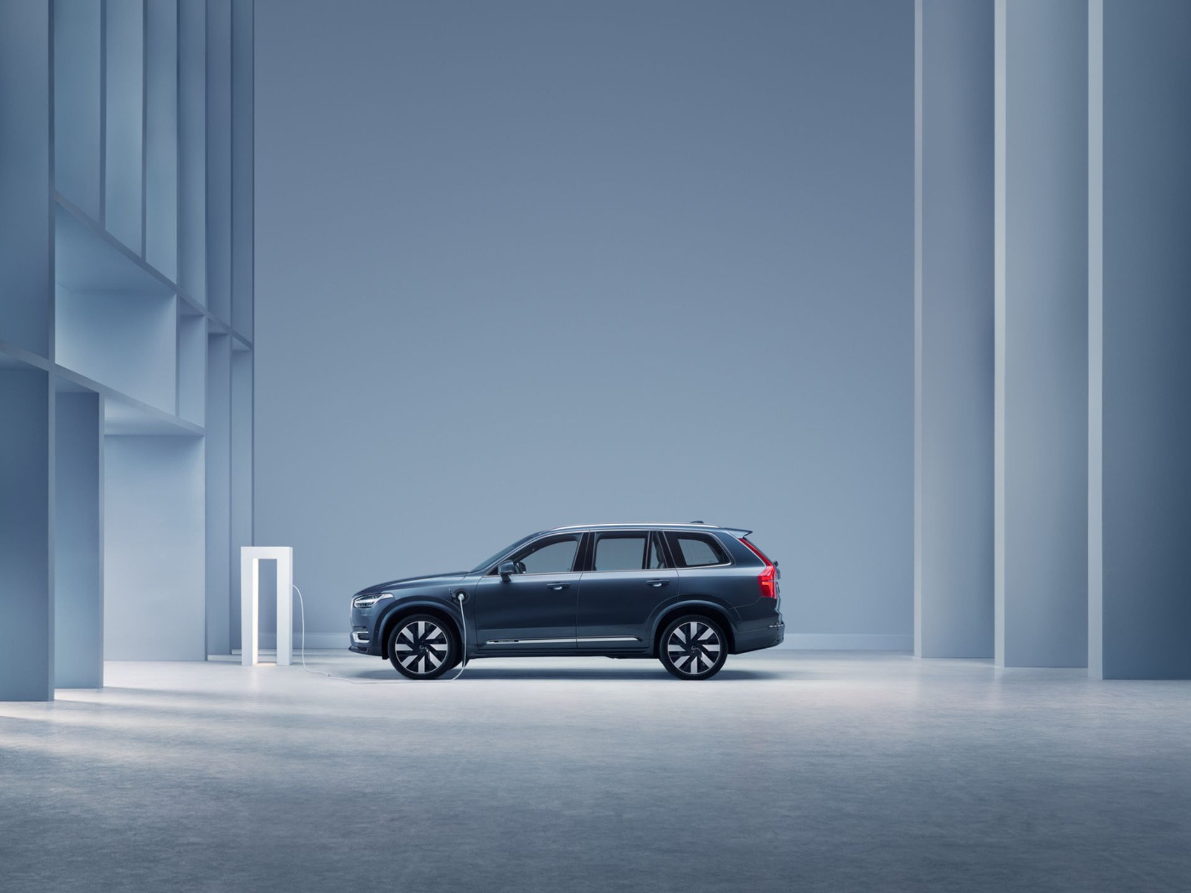 Vue latérale d'un V90 Hybride rechargeable en stationnement, en charge devant un chalet dans la nature scandinave.