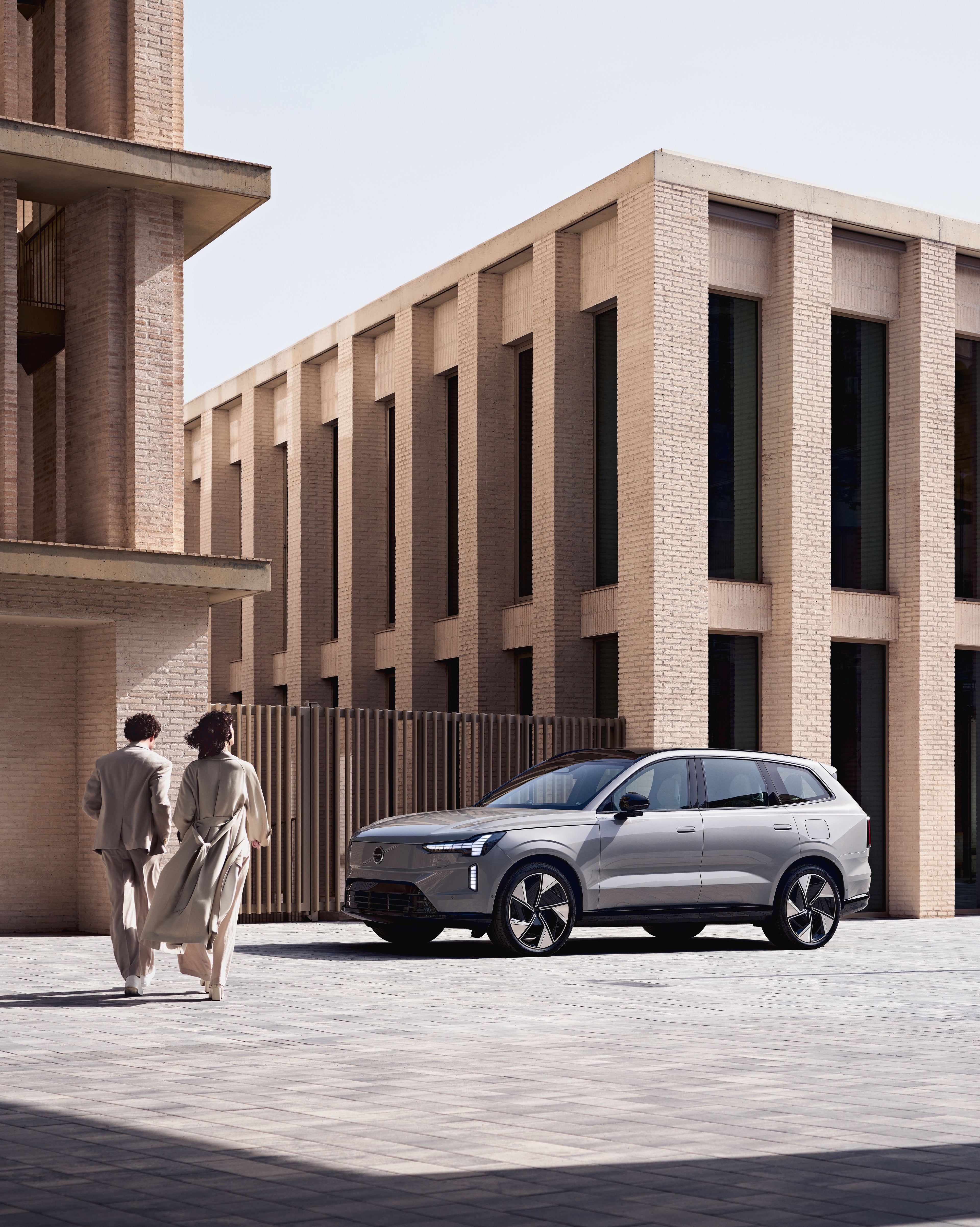A blurred woman stands in the middle of a street with a Volvo EX90 visible behind her.