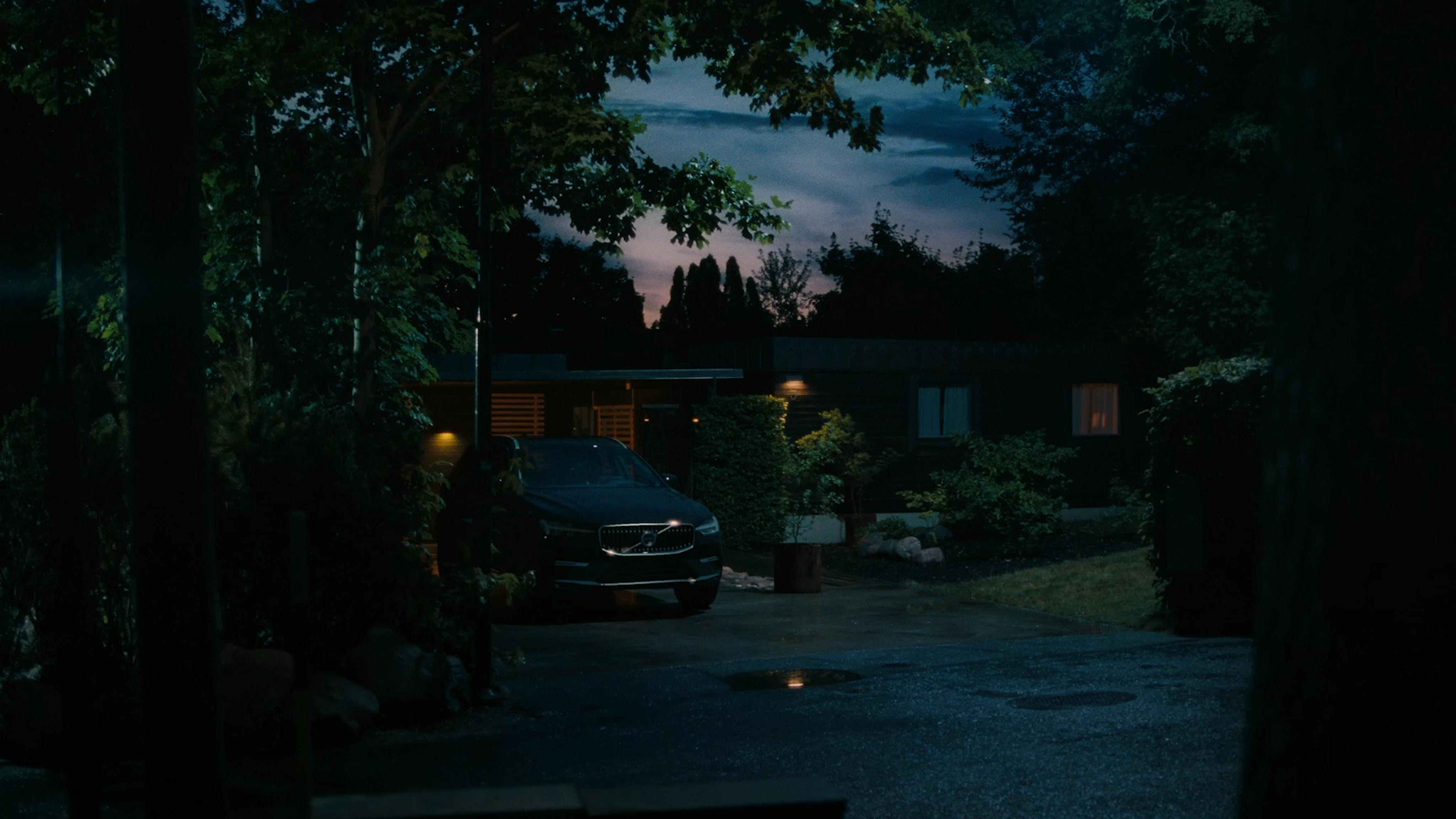 A dark Volvo SUV sits parked on a suburban driveway at dusk.