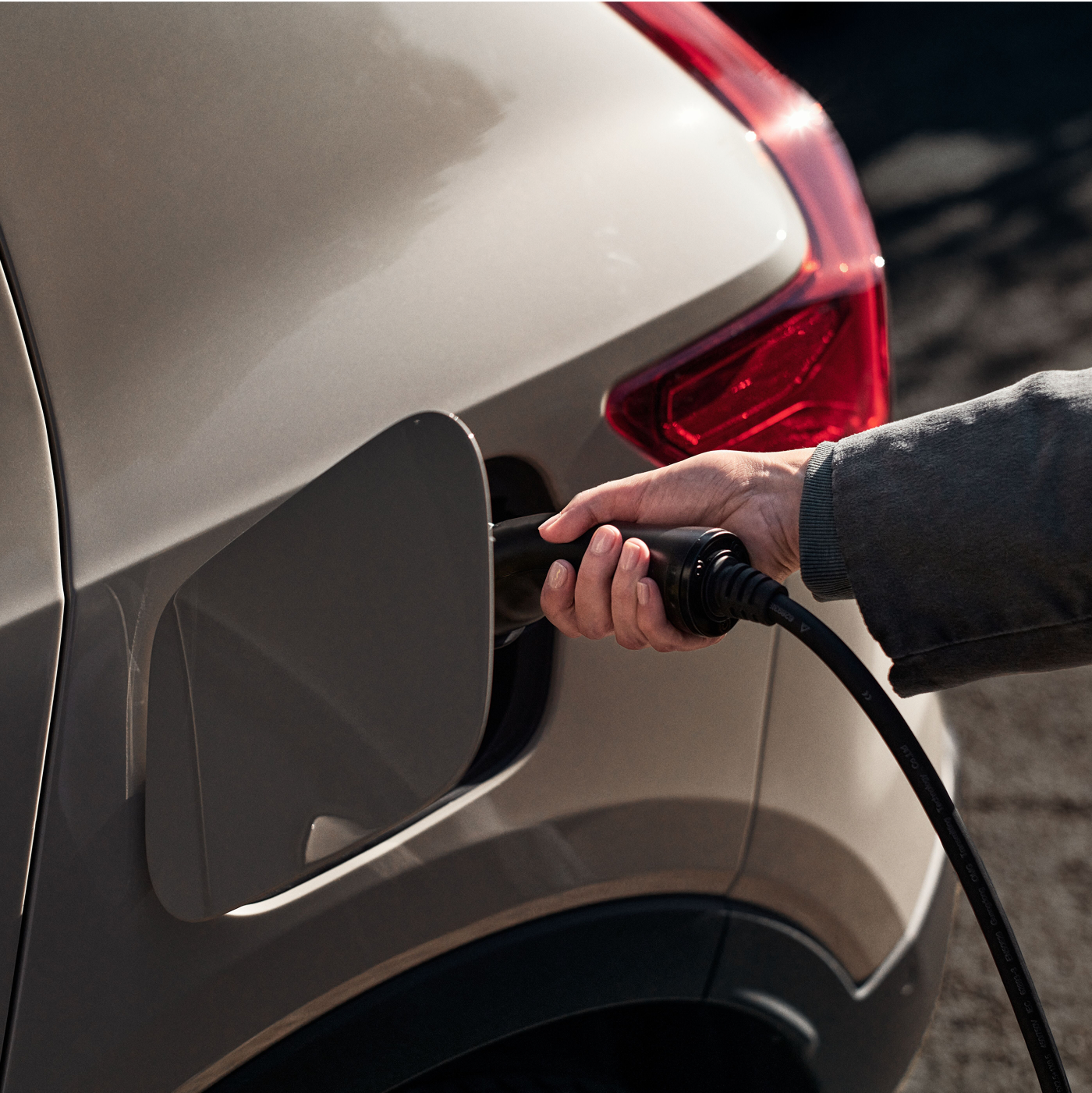 Close up of a hand plugging a charging cable into an electric vehicle.
